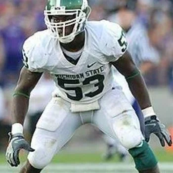 American football player wearing Michigan State uniform number 53, in a ready stance on the field.