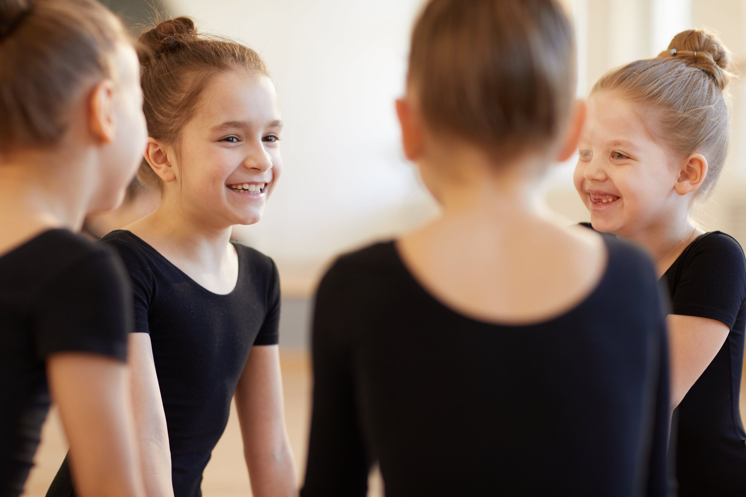 A group of young girls smiling and talking to each other, wearing black leotards.