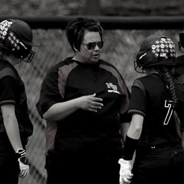 Softball coach speaking to two young players on the field during a game.