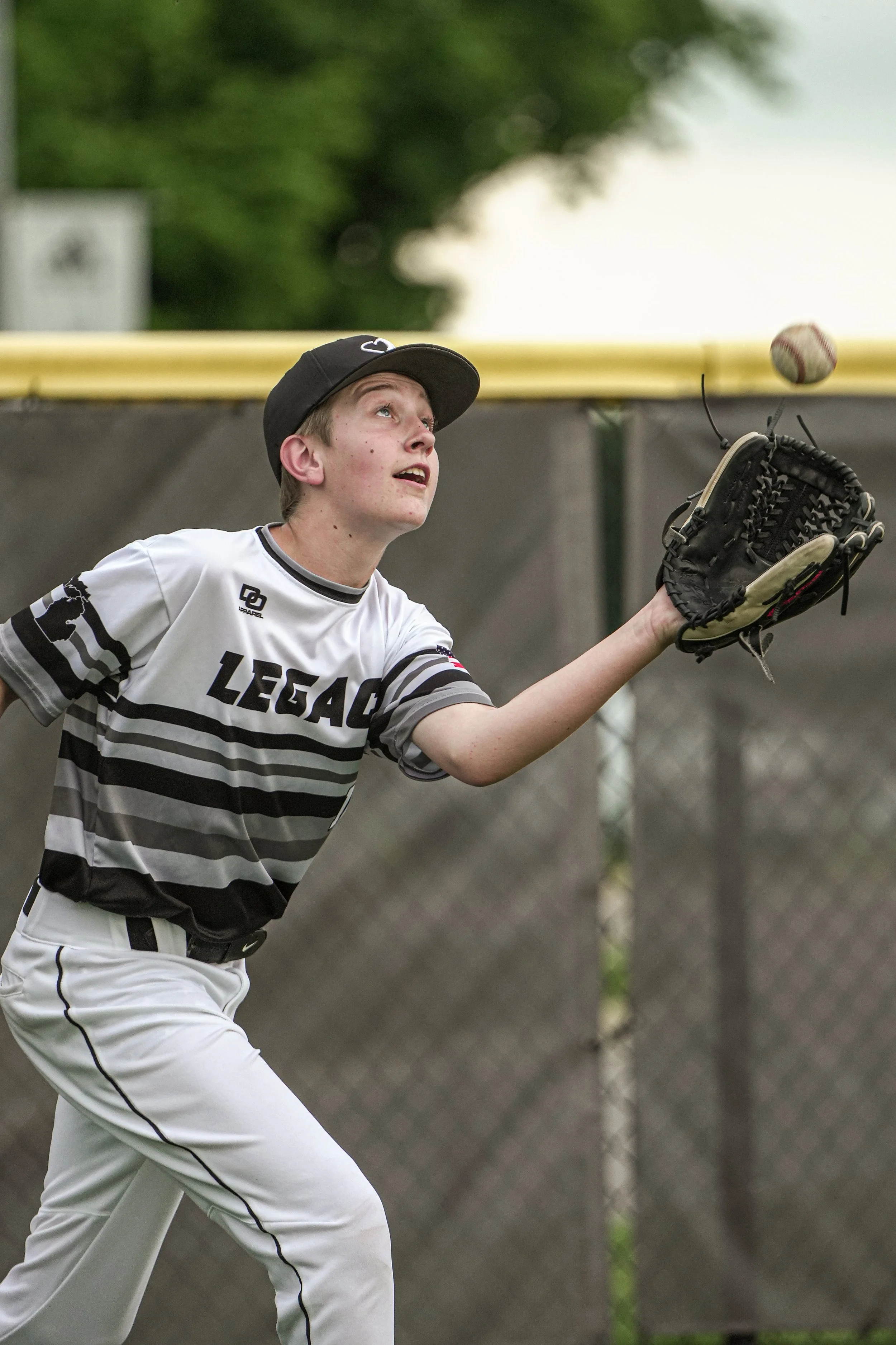 Young baseball player in a uniform catching a ball with his glove during a game.