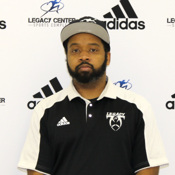 A man with a beard wearing a black and white polo shirt and a white cap, standing in front of a backdrop with logos of Adidas and Legacy Center Sports Complex.