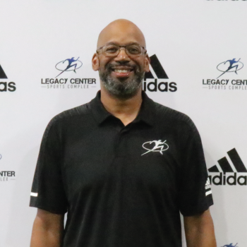 Smiling man wearing a black polo shirt with a sports logo, standing in front of a white backdrop with Adidas and Legacy Center Sports Complex logos.