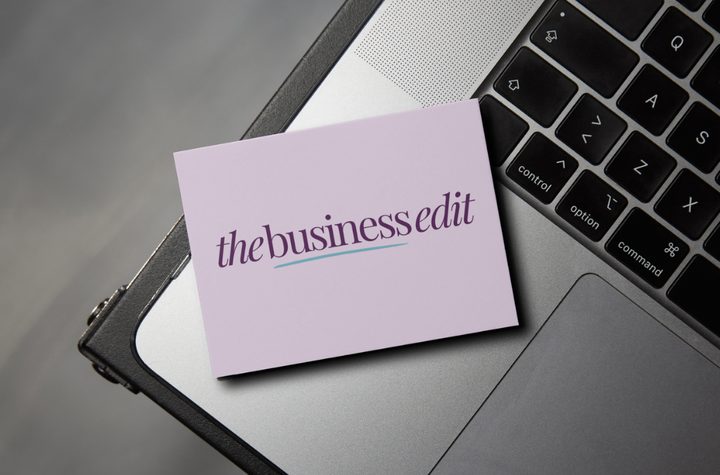 A lilac business card with the text 'the business edit' resting on a silver laptop keyboard.