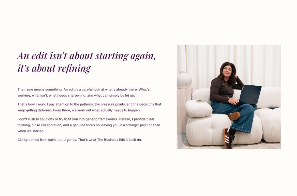 A woman sitting on a white couch with a laptop, smiling, in a well-lit room with curtains.