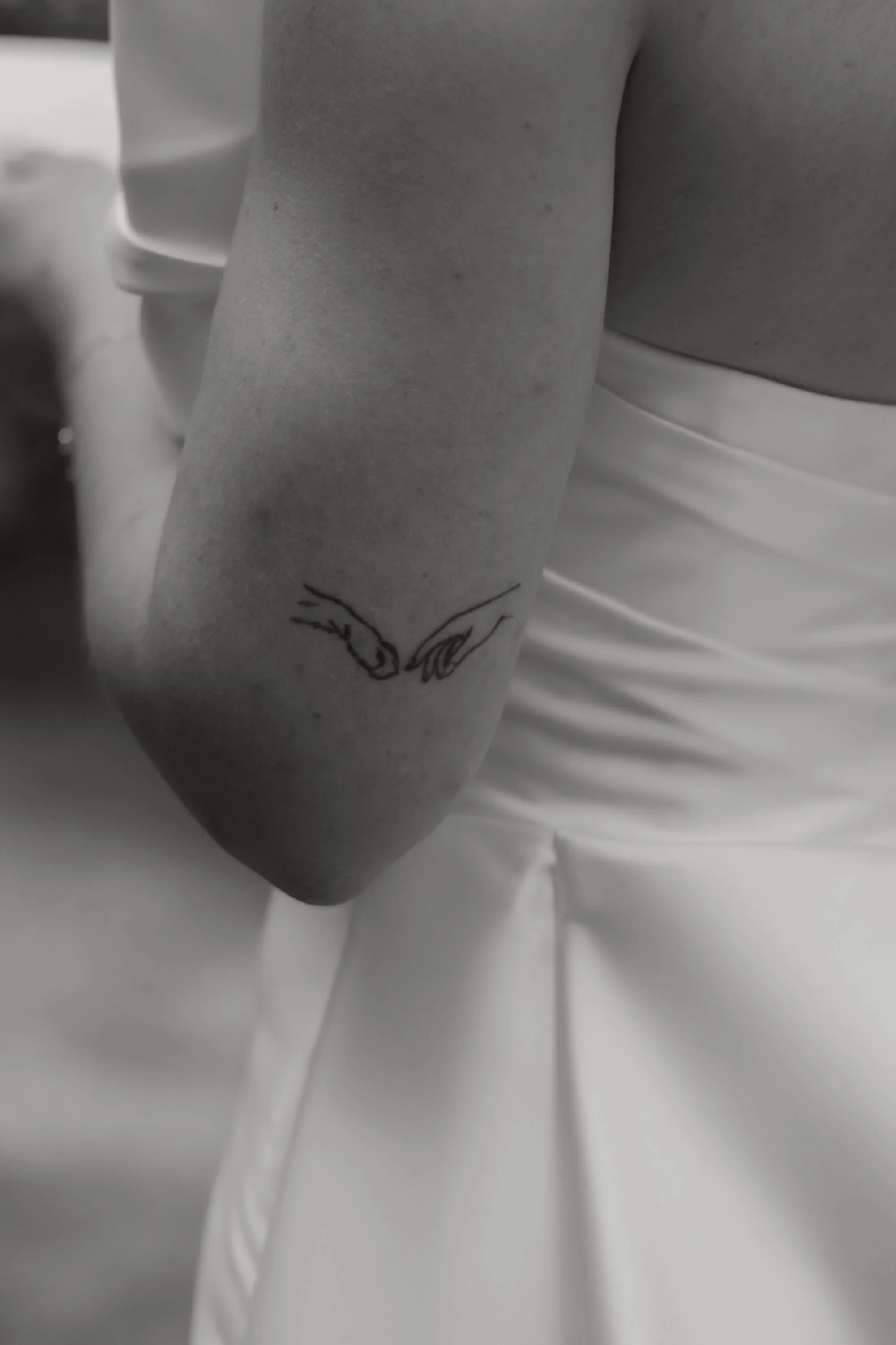 Nahaufnahme eines menschlichen Arms mit Tattoo, neben einer Person in weißem Kleid, im Schwarz-Weiß-Foto.