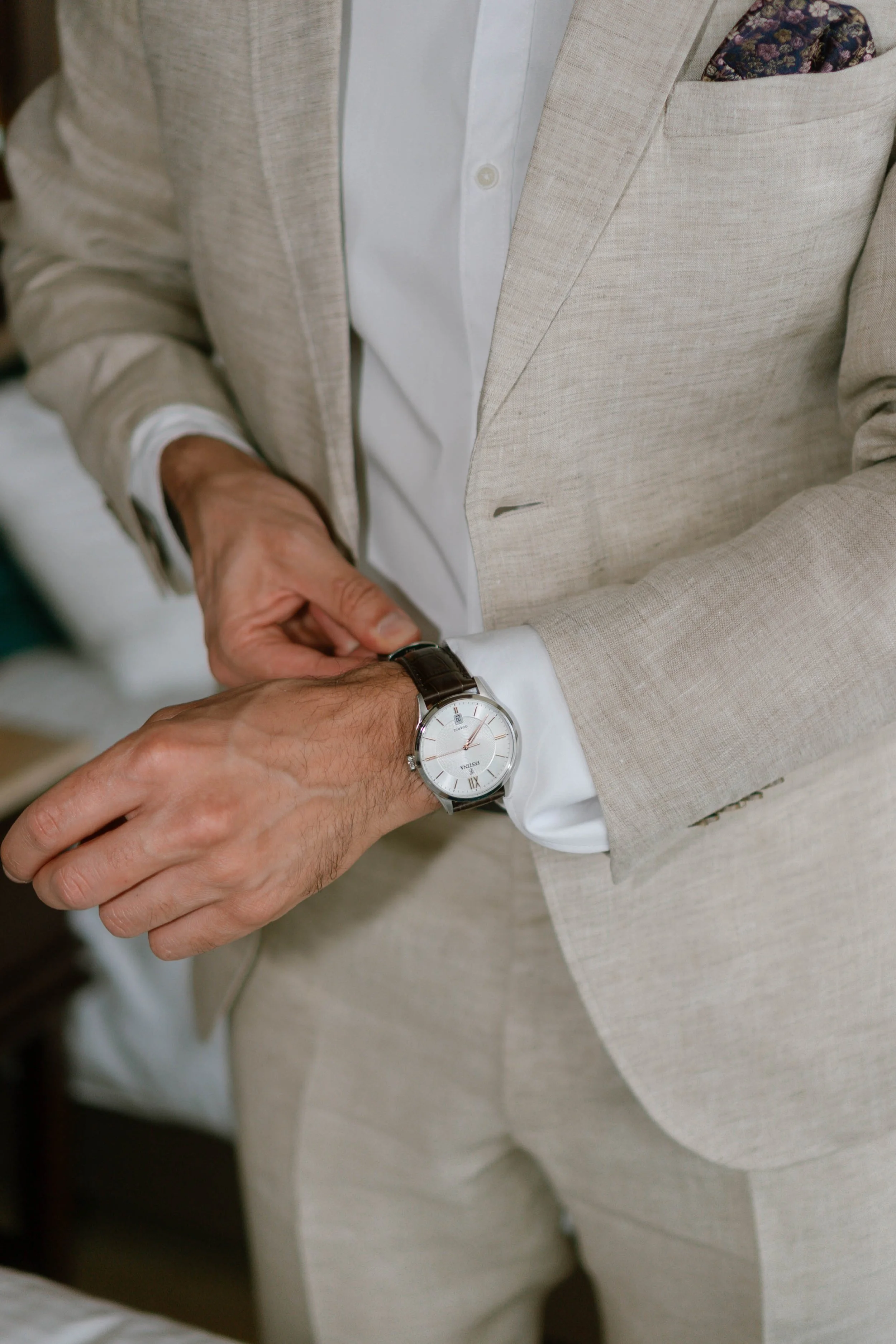 Ein Mann in einem hellen Anzug stellt die Uhr an seinem Handgelenk, während er sich auf einen Termin oder eine Verabredung vorbereitet.