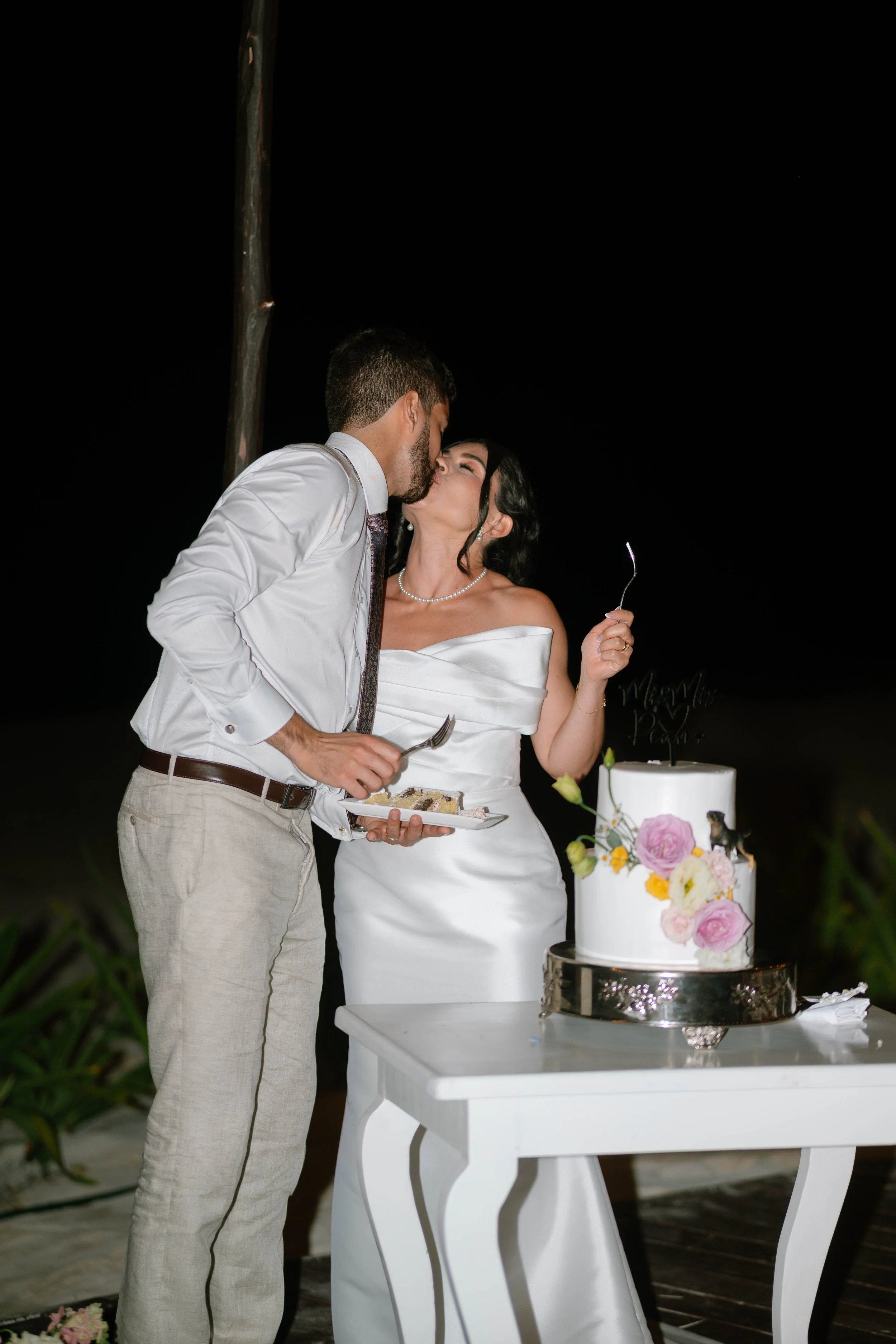 Ein Paar bei einer Hochzeit küsst sich vor einer Hochzeitstorte bei Nacht.