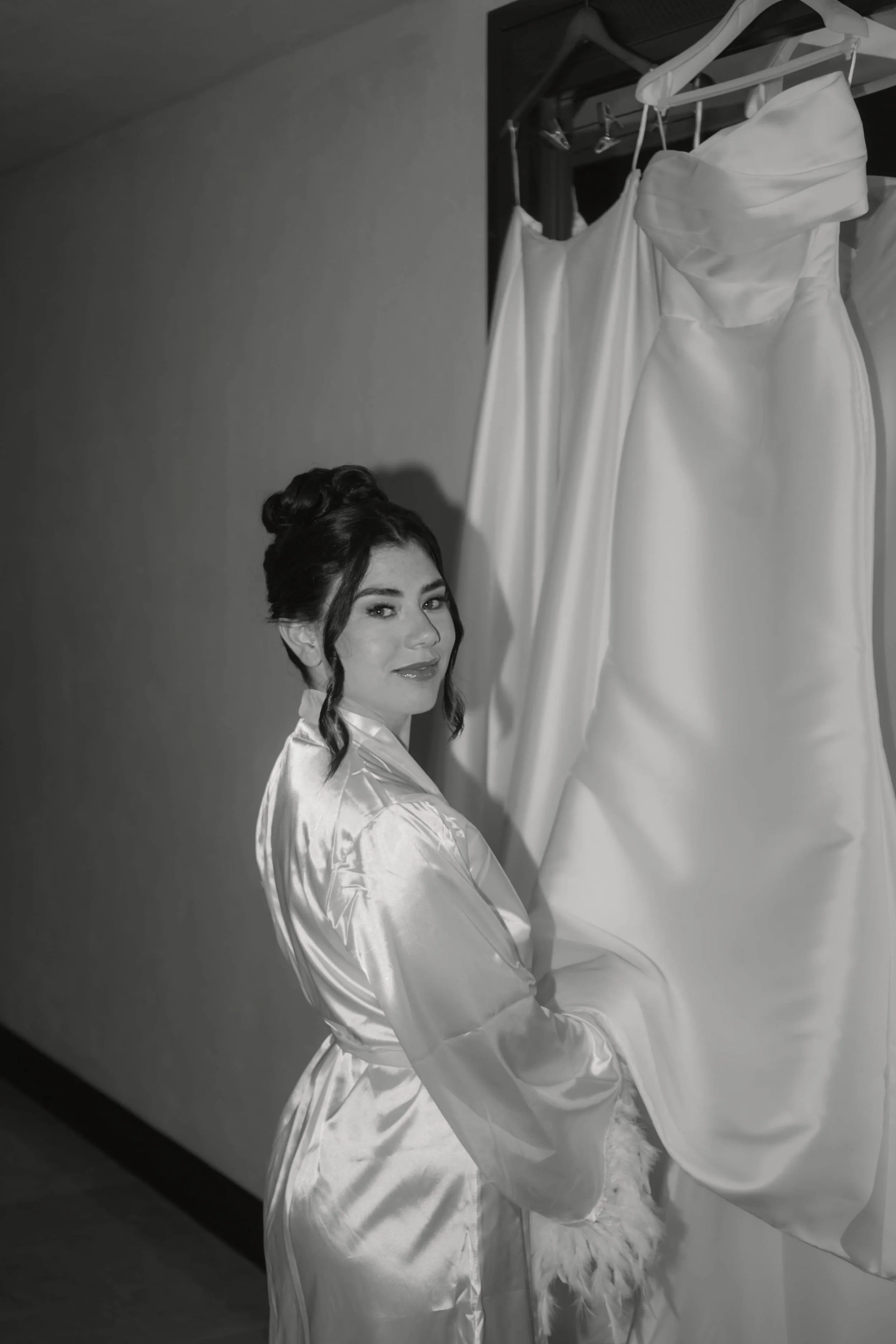 Junge Frau in Seidenkimono vor aufgehängten weißen Brautkleidern.