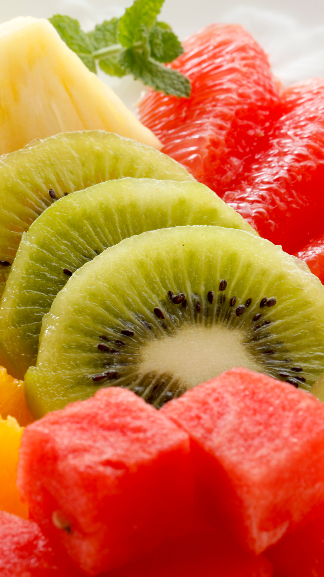 Close-up of sliced kiwi, grapefruit, and watermelon with a sprig of mint on top.