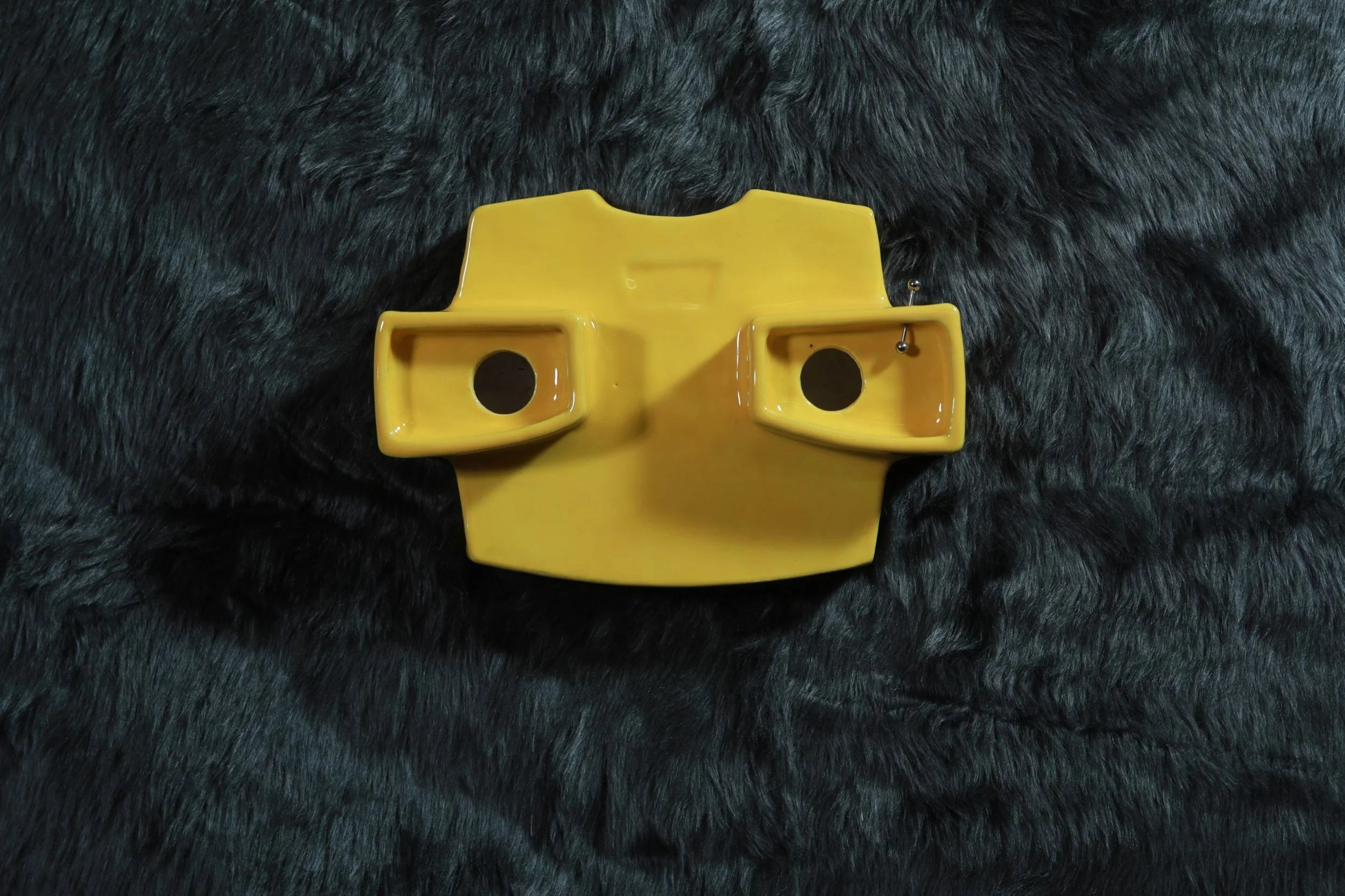 Yellow ceramic representation of a viewfinder on a black furry surface.