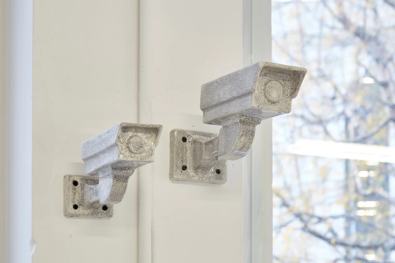 White ceramic representation of CCTV cameras mounted on a wall near a window.