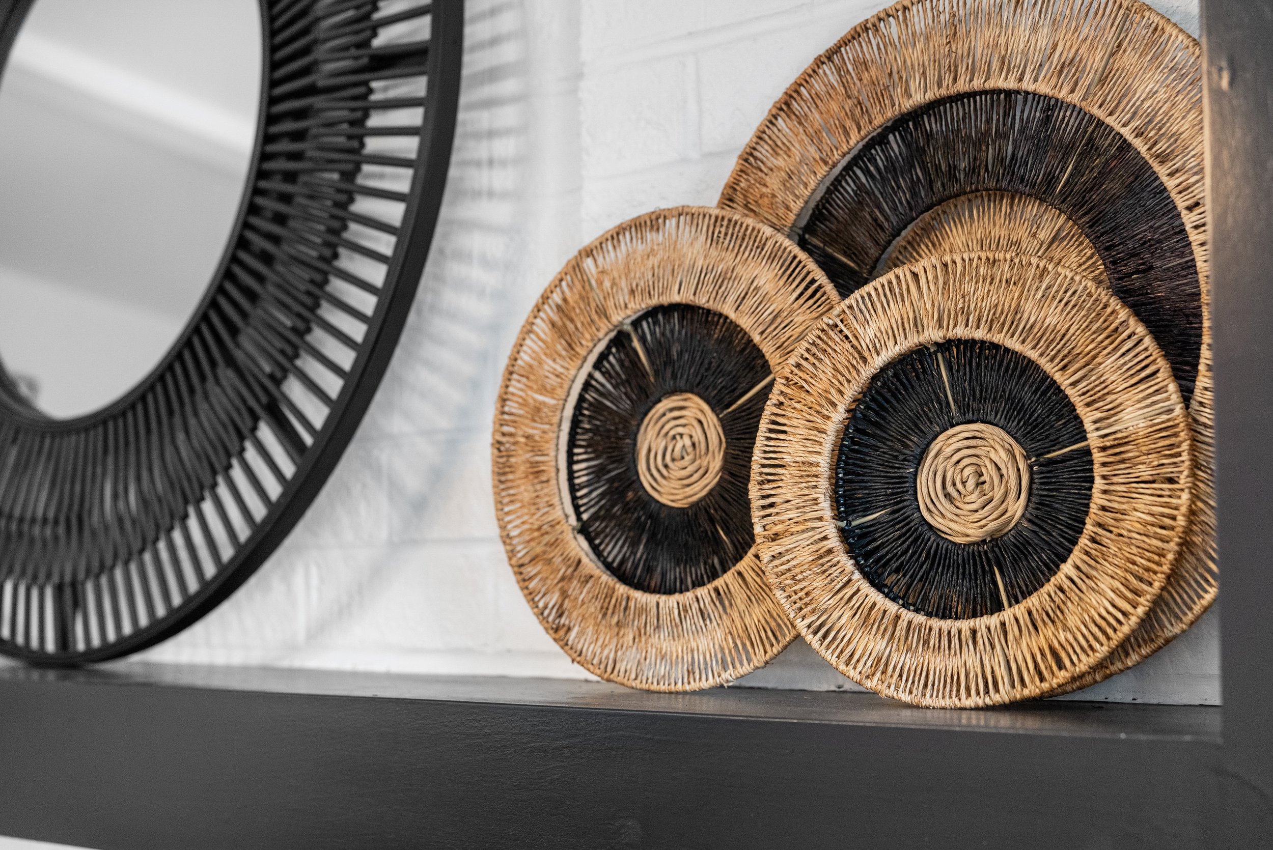 Decorative round wall art pieces made of woven natural and black materials, leaning against a white brick wall.