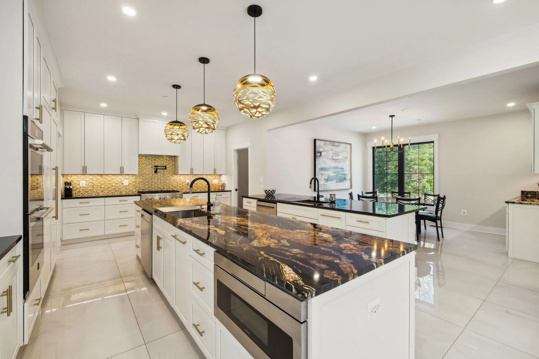 Modern kitchen with white cabinets, black countertops, pendant lights, and a dining area with black chairs and a large window.