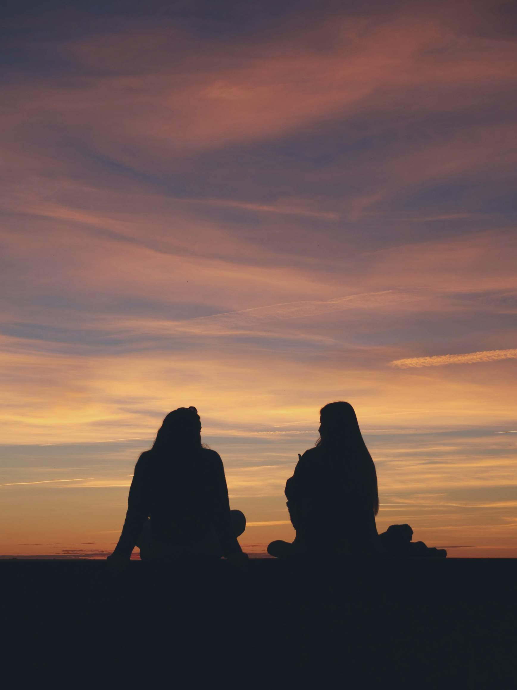 Silhouettes of two women sitting in front of a sunset talking amicably
