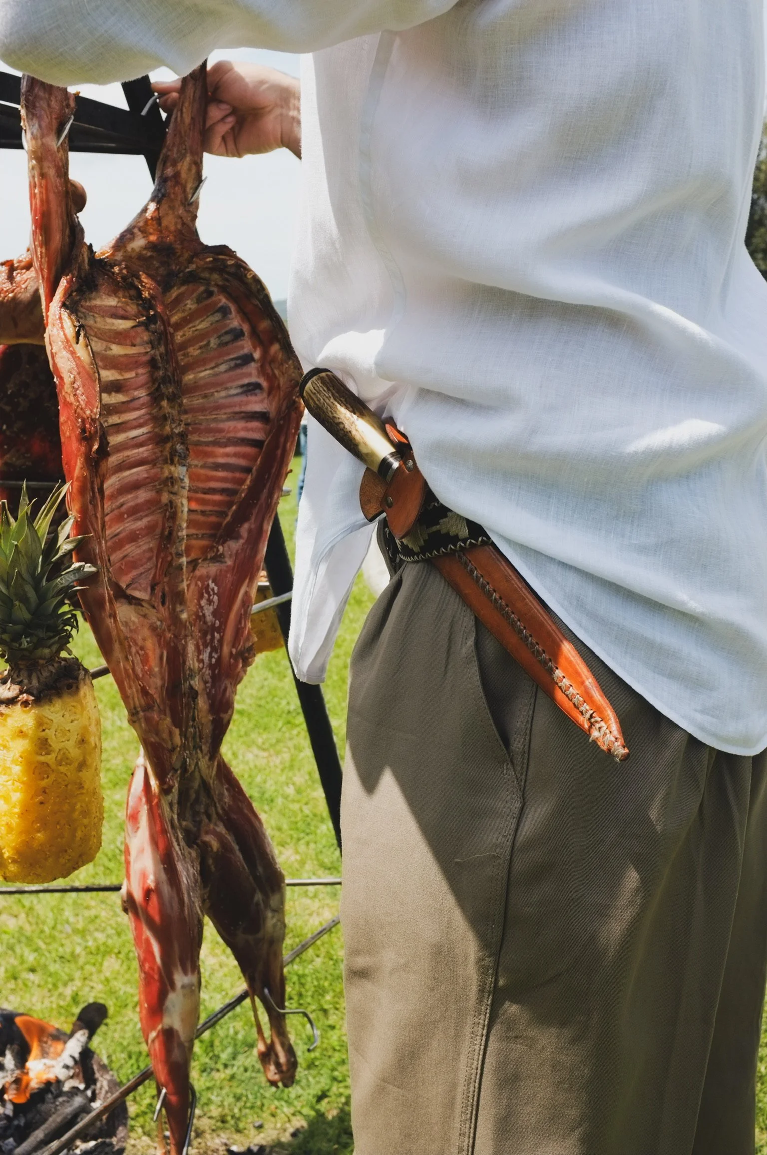 Persona che tiene in mano un pesce aperto, probabilmente durante una grigliata, con un coltello di caccia nella cintura