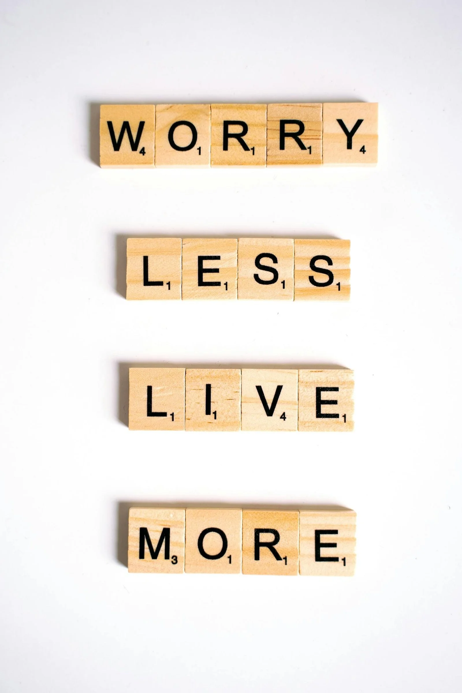 Wooden letter tiles arranged vertically to spell ‘Worry Less Live More’ on a white background.