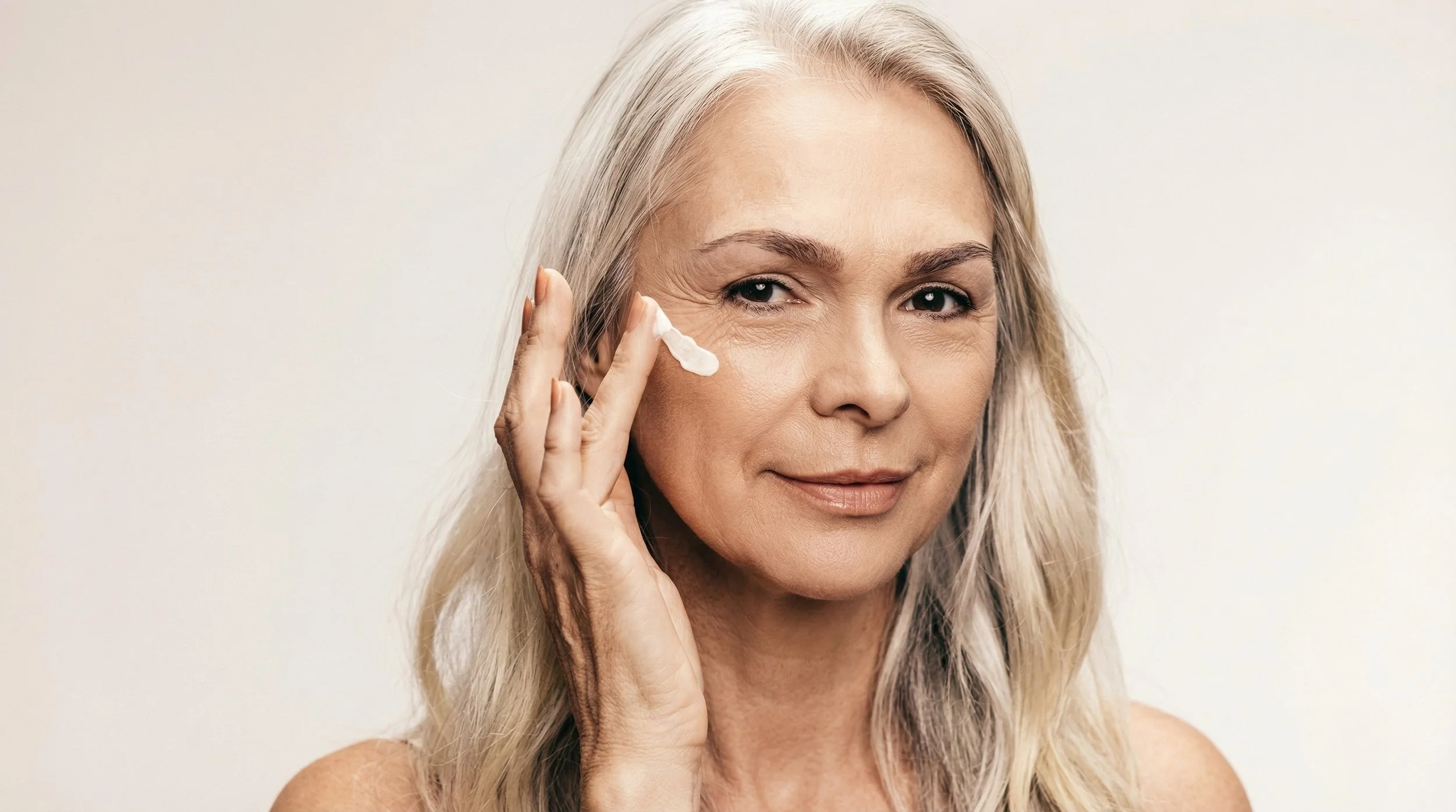 Femme âgée appliquant une crème sur sa joue