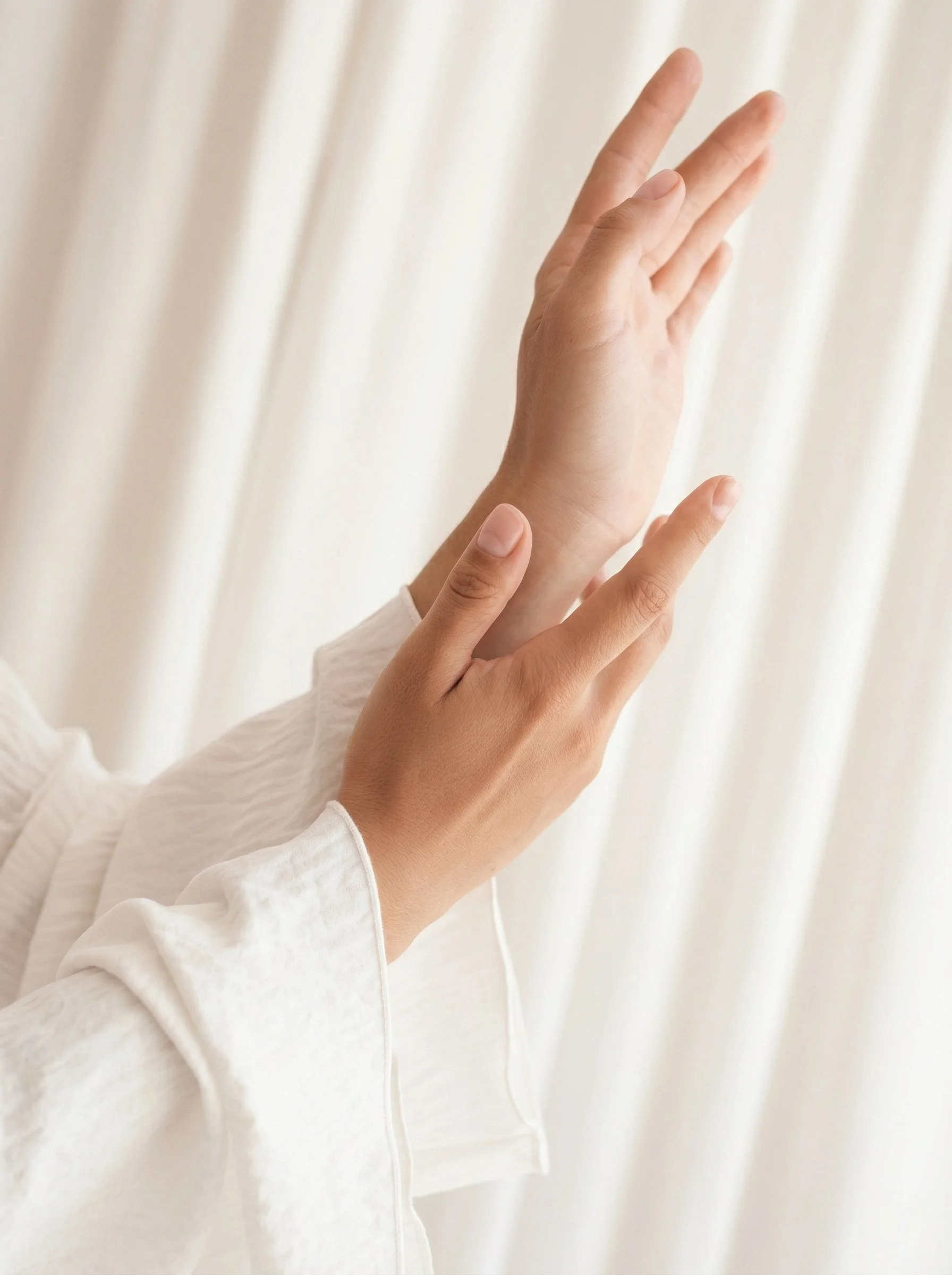 Deux mains, une plus grande et une plus petite, en position de geste de salut ou de prière contre un rideau blanc.