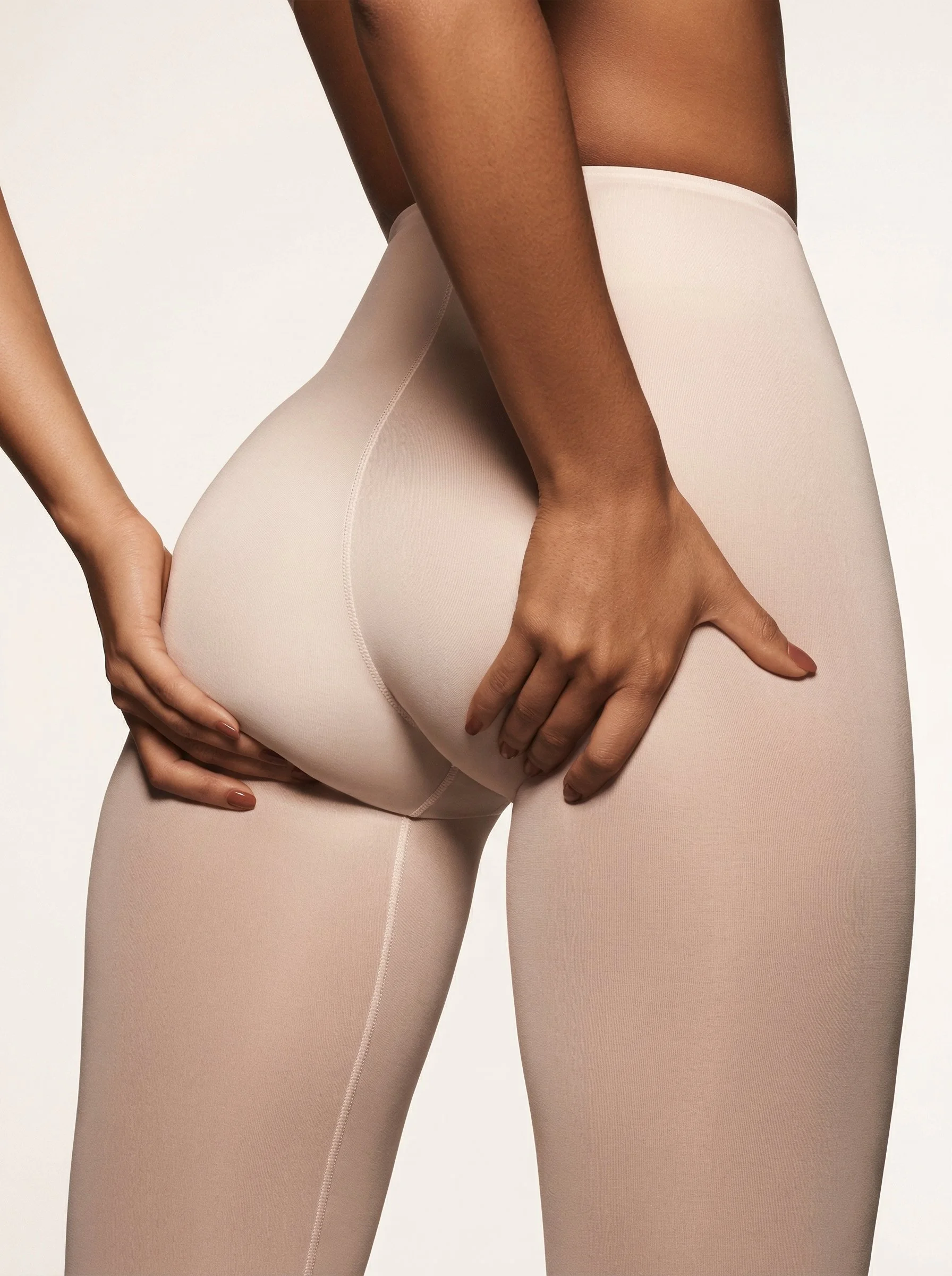Close-up d'une personne portant des leggings beige clair, tenant le haut de la jambe avec une main, photographiée en gros plan.