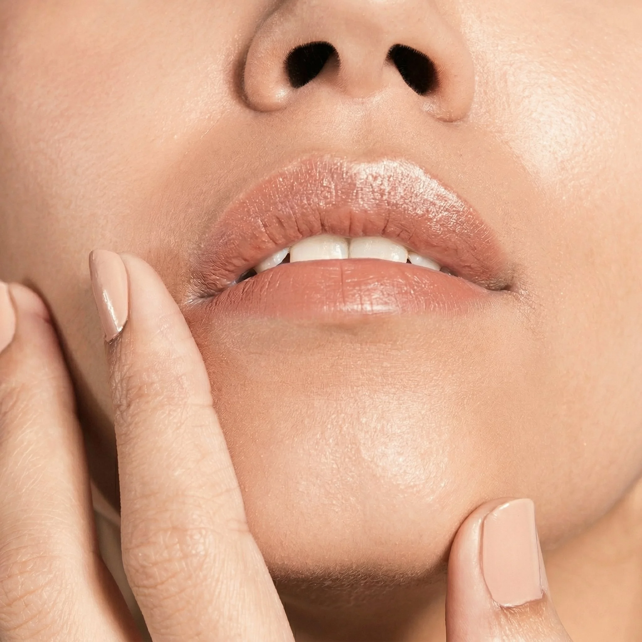 Gros plan du visage d'une femme, mettant en valeur ses lèvres, son nez et ses doigts avec des ongles impeccables, alliant naturel et élégance.