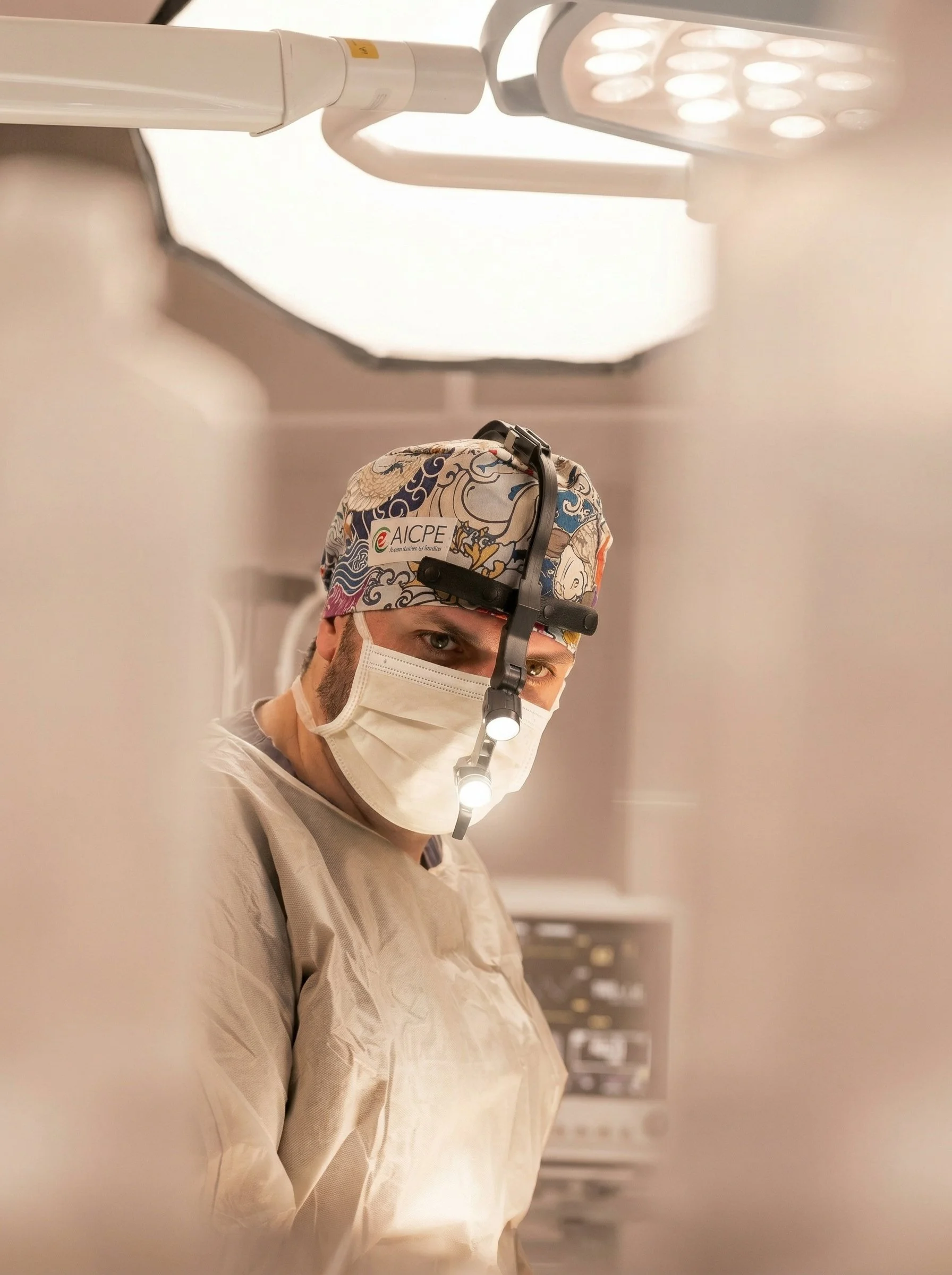 Un médecin ou un professionnel de la santé portant une tenue chirurgicale, un masque, une casquette avec le logo AI fome, une lampe frontale, dans un environnement médical.