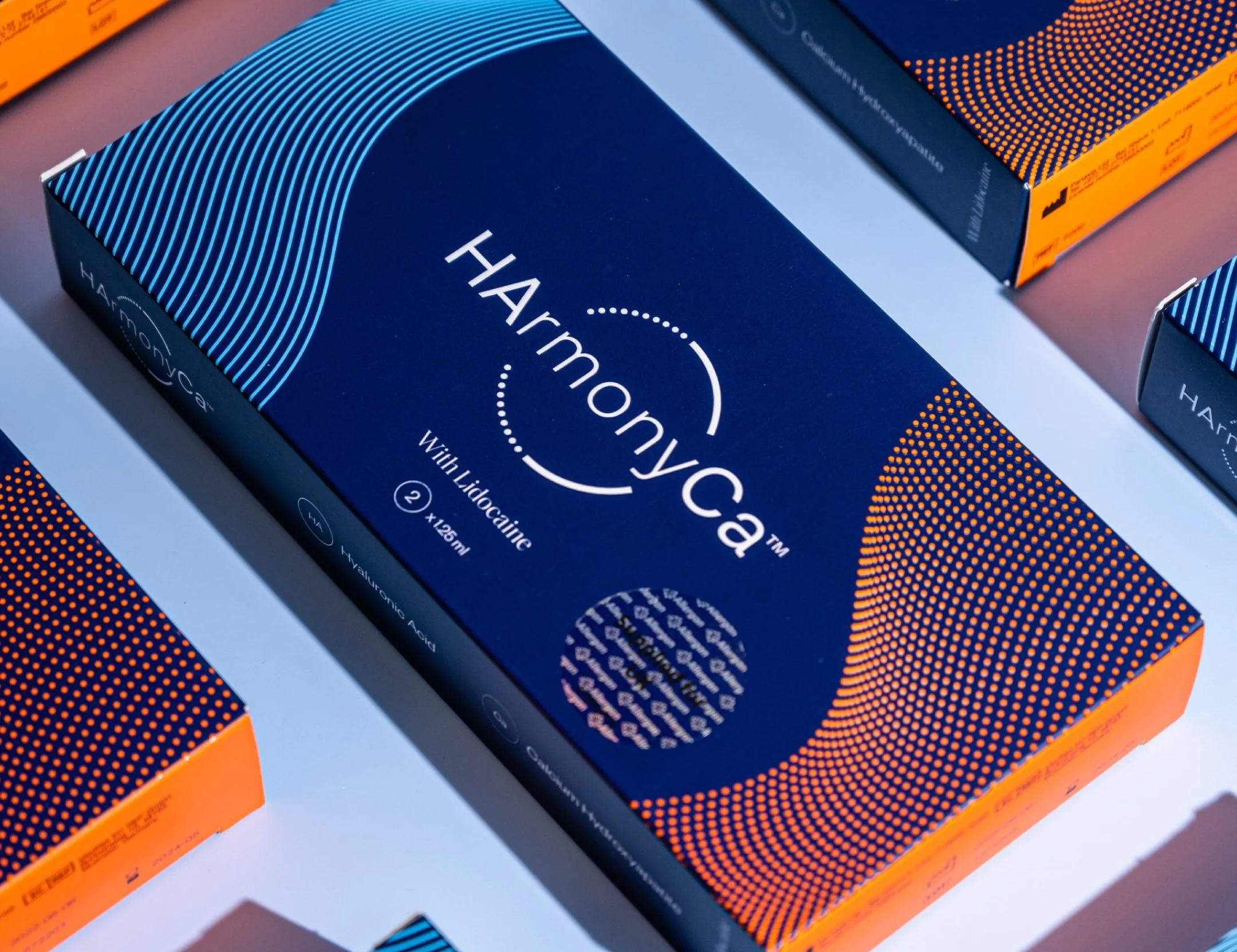 Boîte de médicament Harmonyca avec lidocaïne, 126 ml, sur fond blanc avec autres boîtes similaires.
