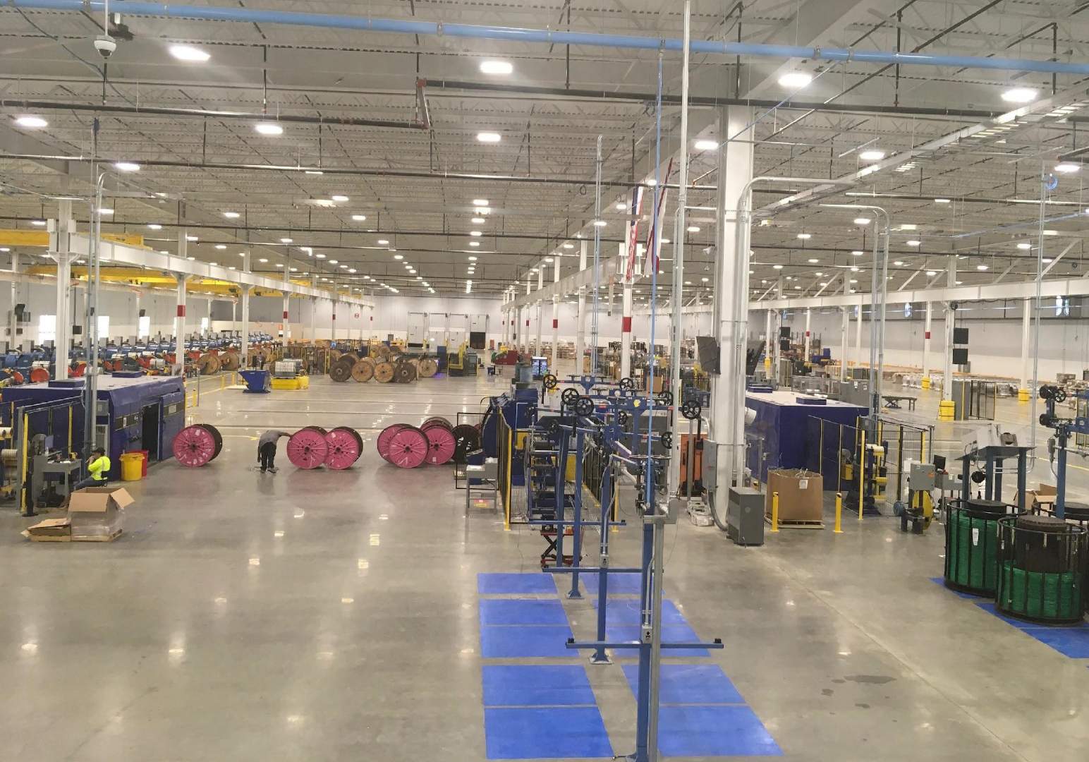 An expansive industrial warehouse interior with machinery, equipment, and workers, likely a manufacturing or assembly plant.