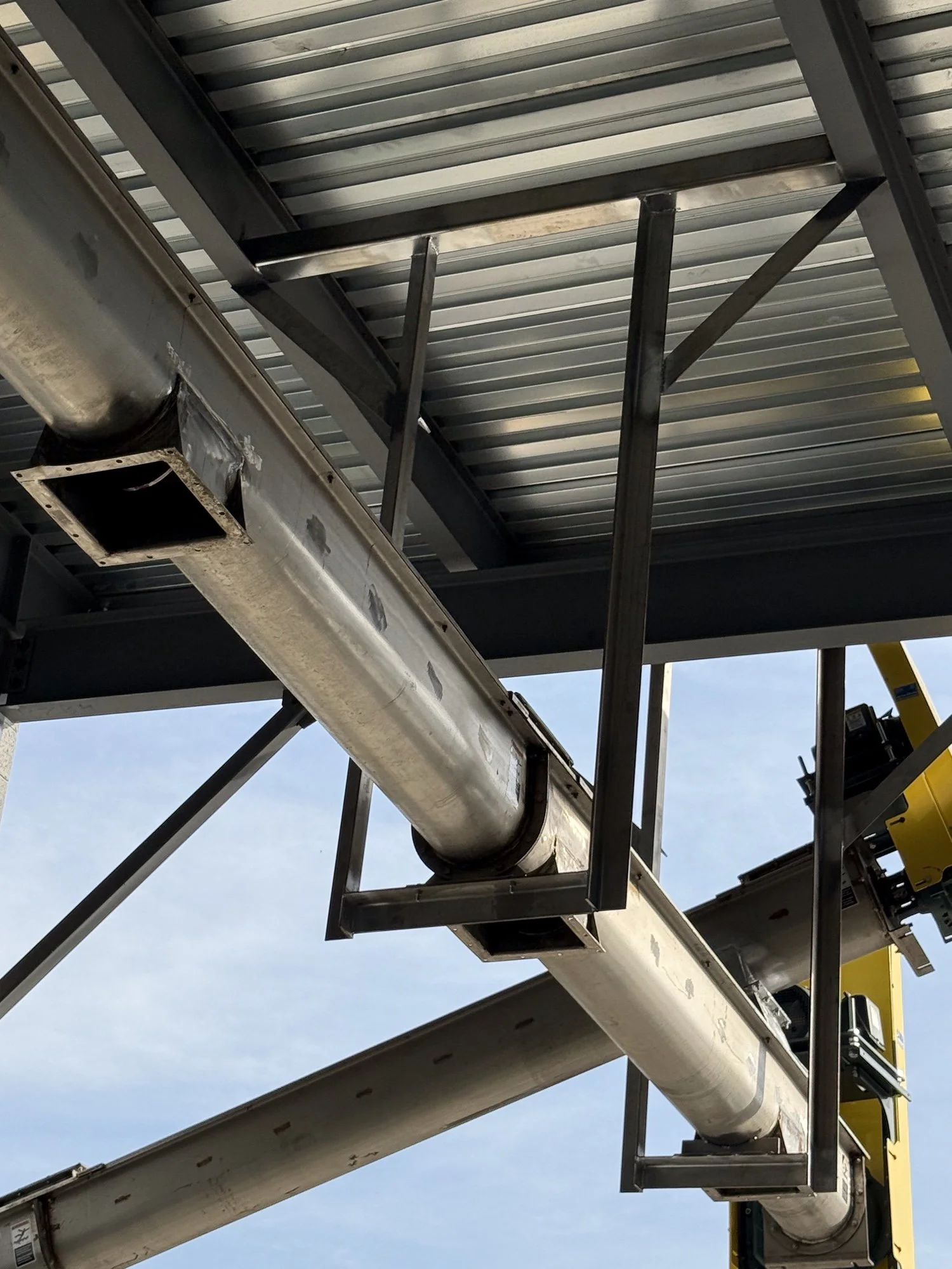 Close-up of industrial air duct and metal framework inside a building with a metal roof.