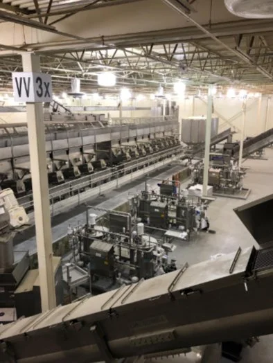 View of an industrial factory with machinery, conveyor belts, and a large storage area, seen from an elevated position.