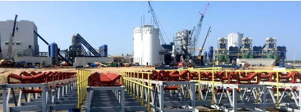 Industrial construction site with large cranes, pipes, and machinery, and a partially built structure in the background.