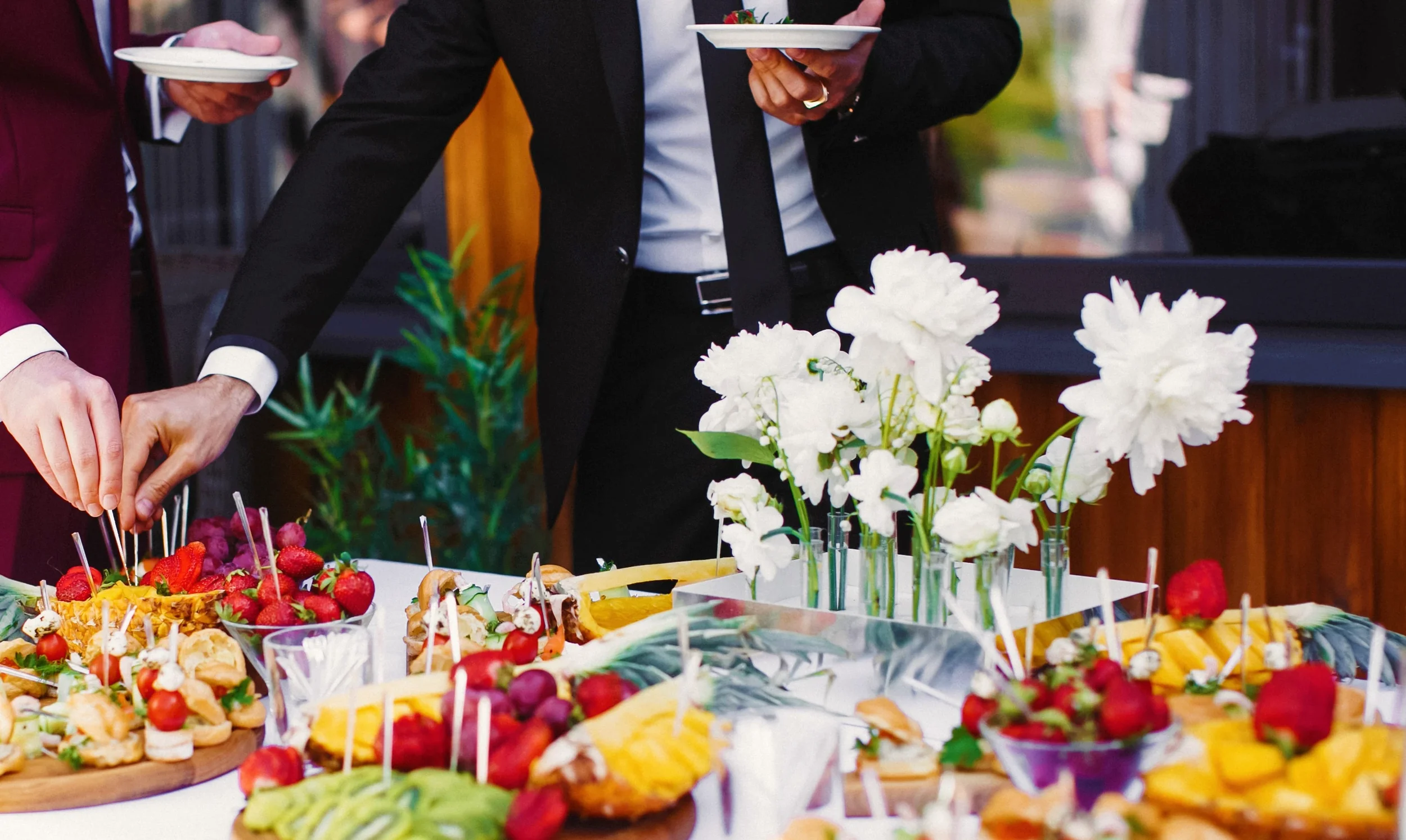 Menschen bei einem Buffet mit frischem Obst und Blumen.