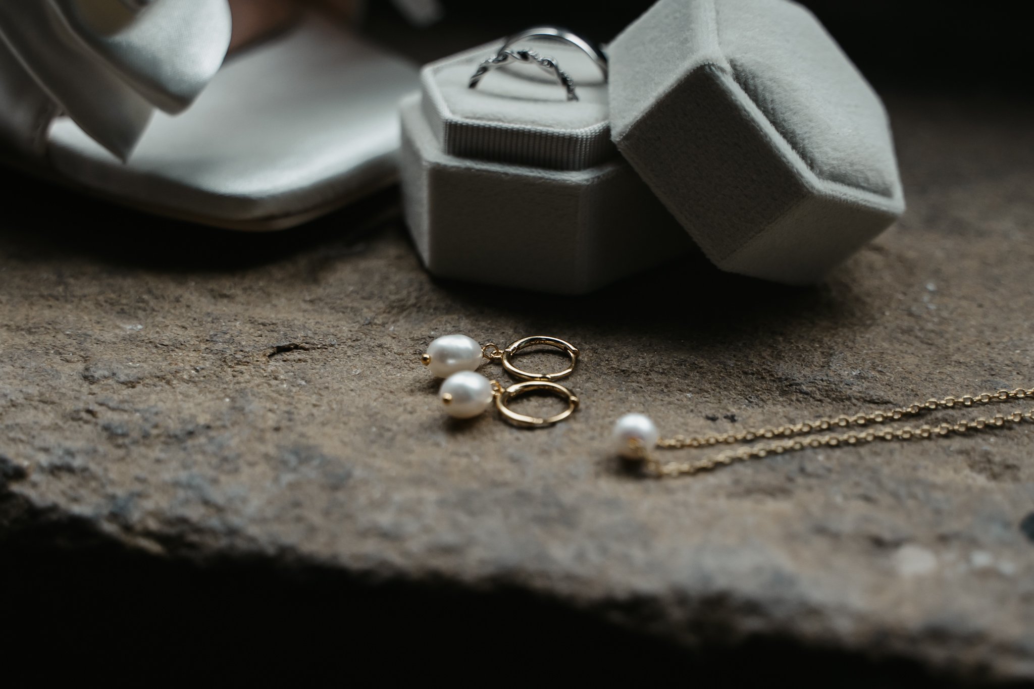 A pair of pearl and gold hoop earrings, a pearl necklace, and a ring in a fabric jewelry box, with a white satin cloth partially visible, on a textured surface.