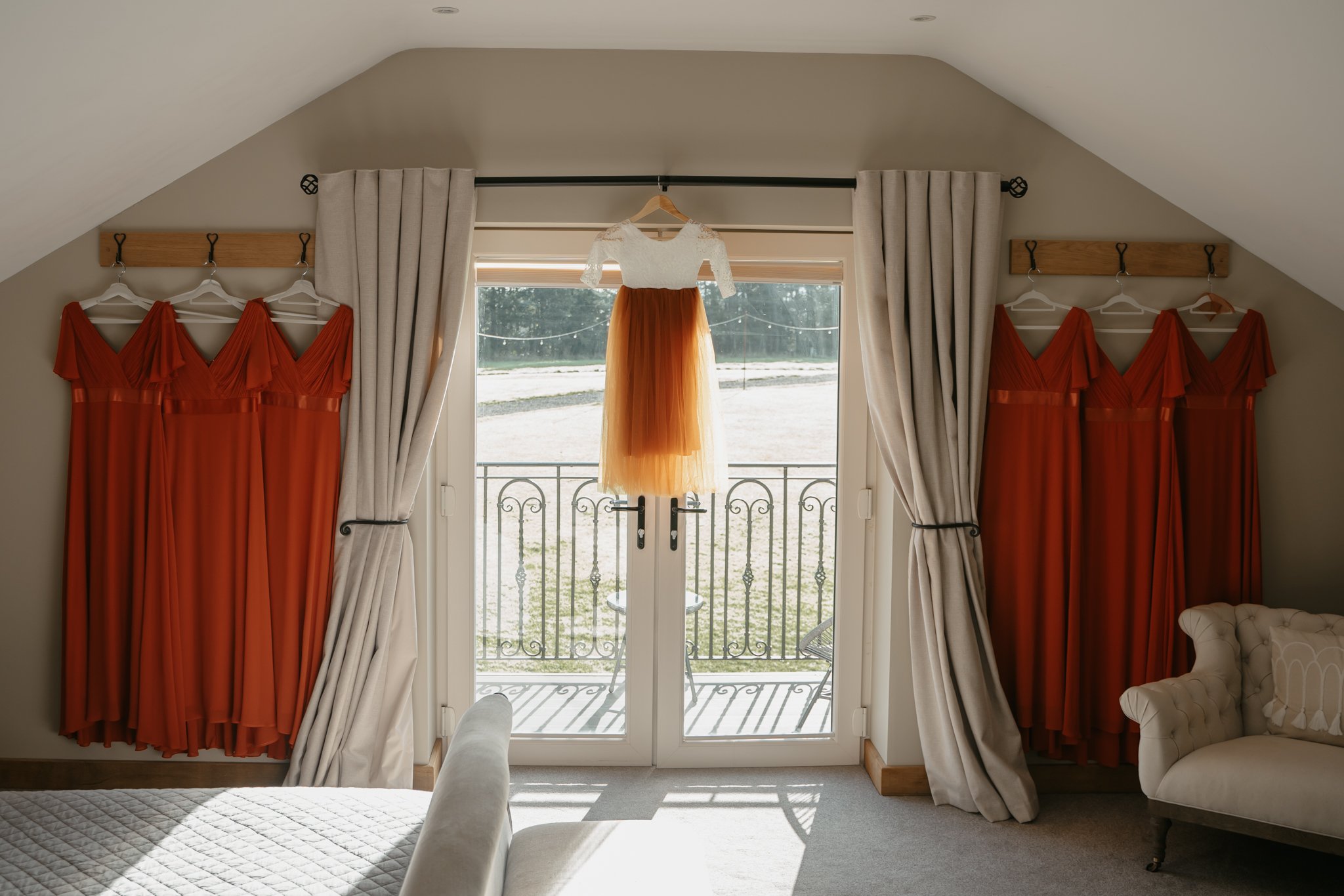 A children's dress with a white lace top and a tulle skirt in shades of orange hanging in front of glass doors on a balcony, with four matching orange dresses hanging on either side.