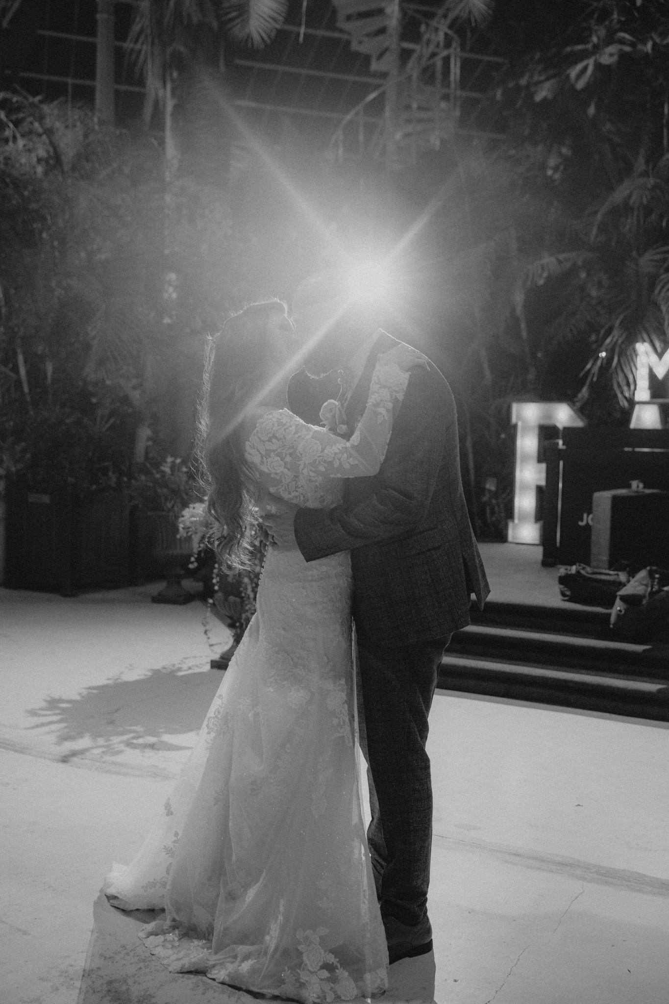 A black and white photo of a bride and groom dancing closely at their wedding, with a bright light behind them creating a silhouette effect.