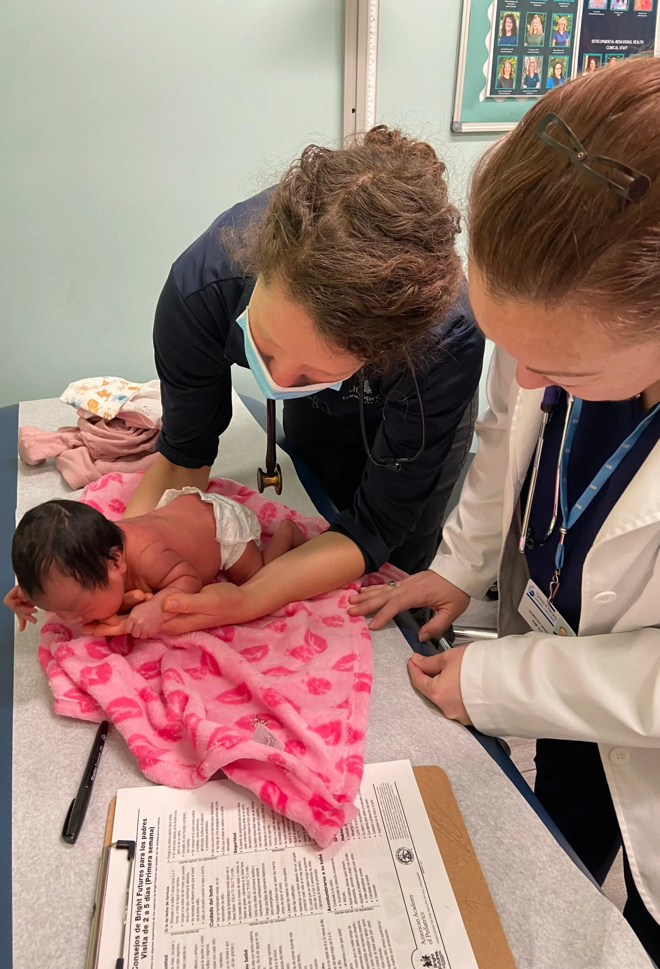 Medical professionals attending to a newborn baby on a pink blanket in a hospital room.