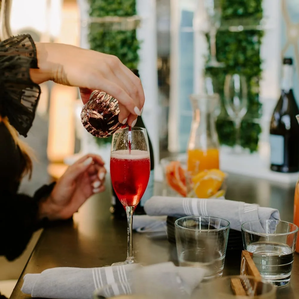 A person pouring red sparkling wine into a champagne flute on a dining table set for a meal.