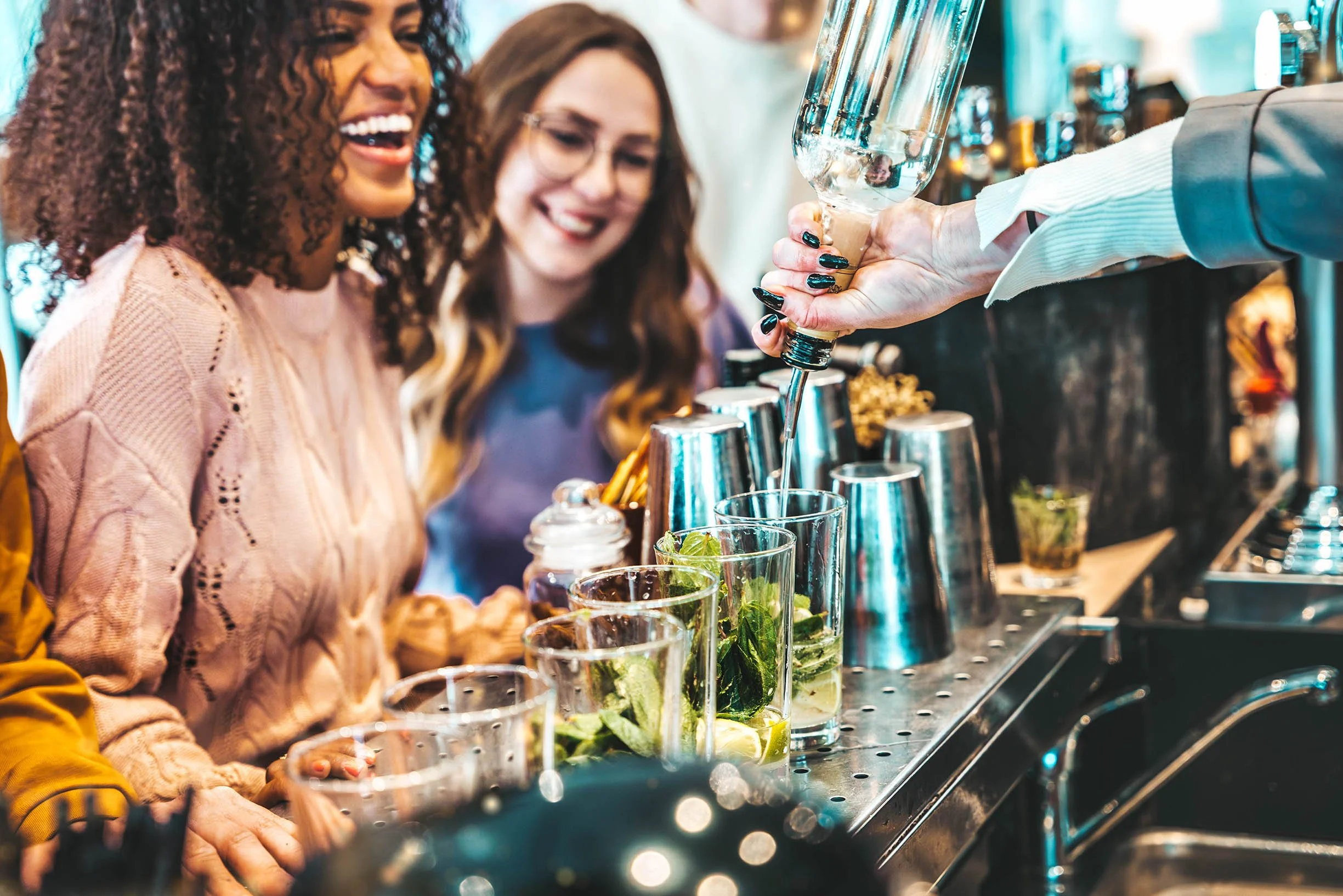 People at a bar enjoying drinks, with a bartender pouring a drink into a glass. - Double O London