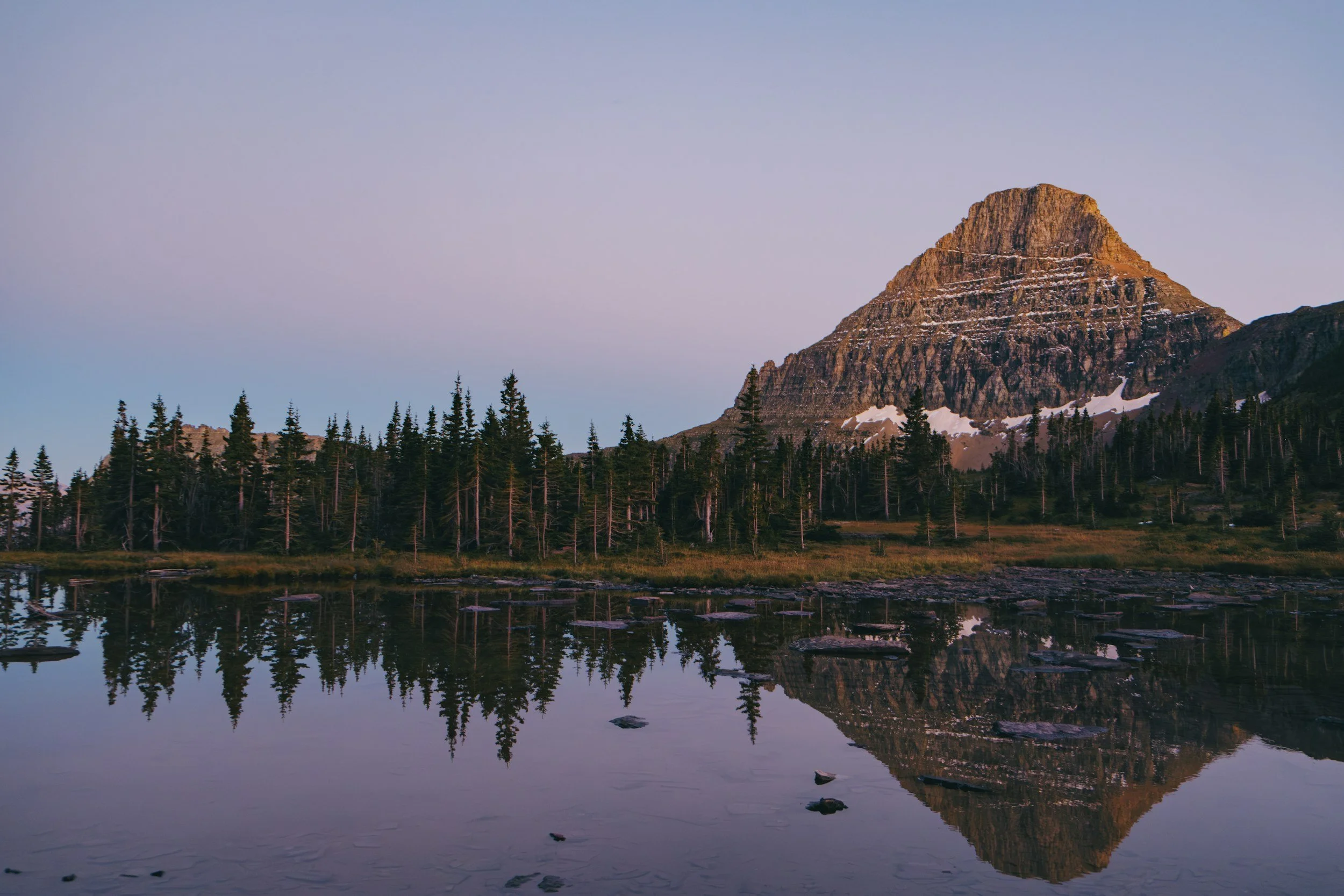 Mountaintop with trees and snow reflected in a lake during sunset