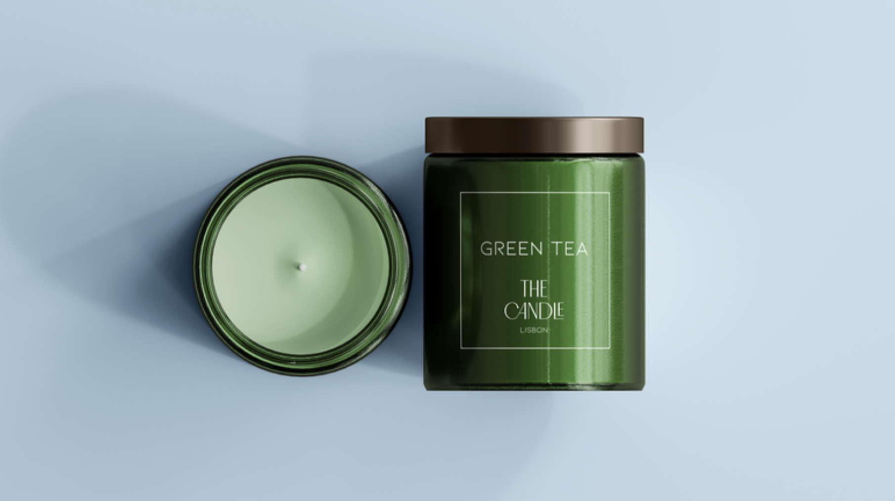 A green candle labeled "Green Tea The Candle" in a green jar with a brown lid, placed on a light blue background.