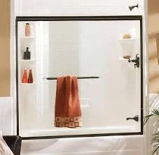 Shower with glass door, orange towel hanging on a bar, and built-in shelves with shampoo and soap