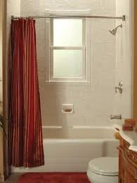 Bathroom with a bathtub, red shower curtain, small window, and toilet.