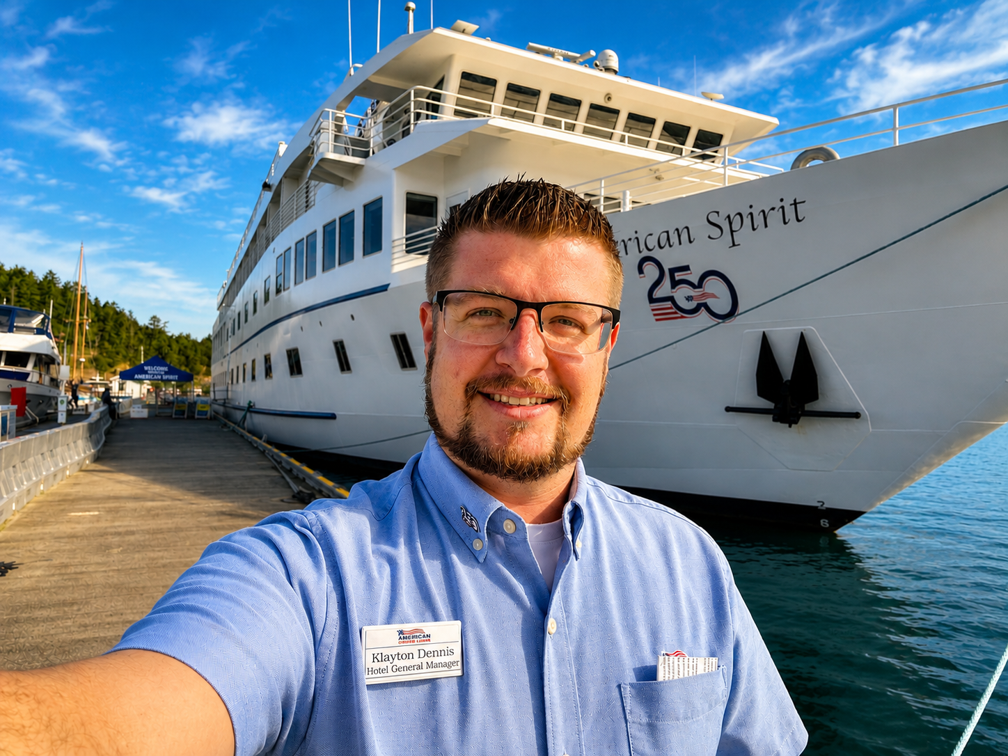 A man with glasses and a beard smiling in front of a large white cruise ship with the name 'American Spirit' at a dock.