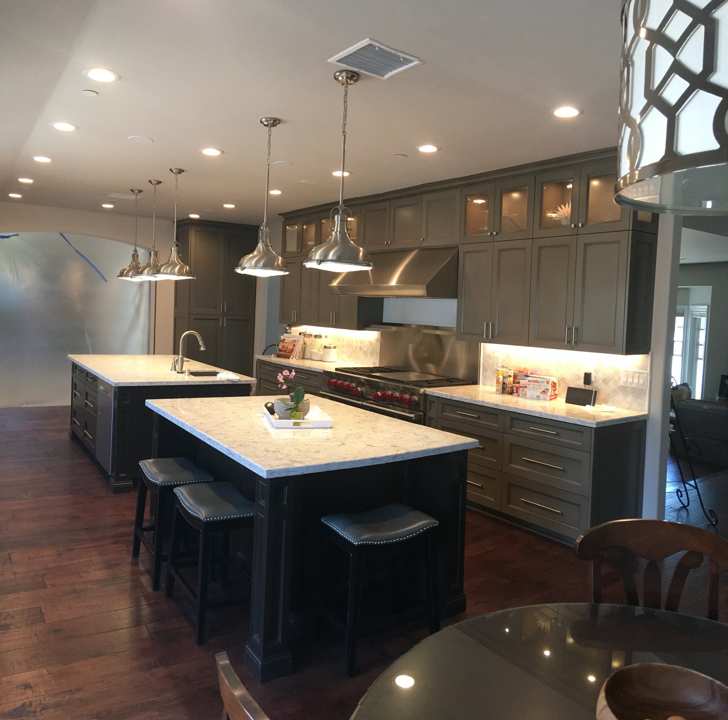 Modern kitchen with dark cabinetry, granite countertops, and a large island with seating. Overhead pendant lights and hardwood floors.