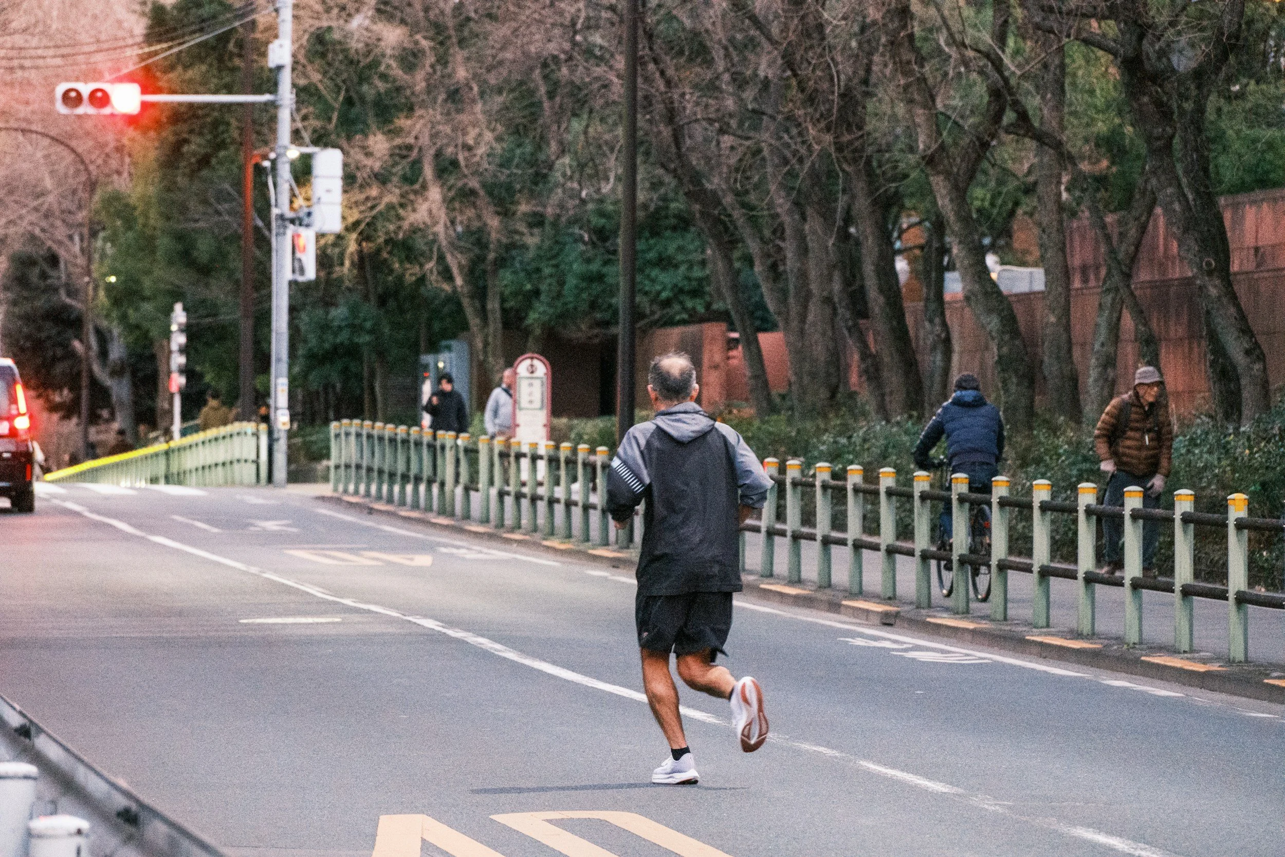 A man jogging on a city street near a traffic light, with pedestrians and a cyclist in the background.