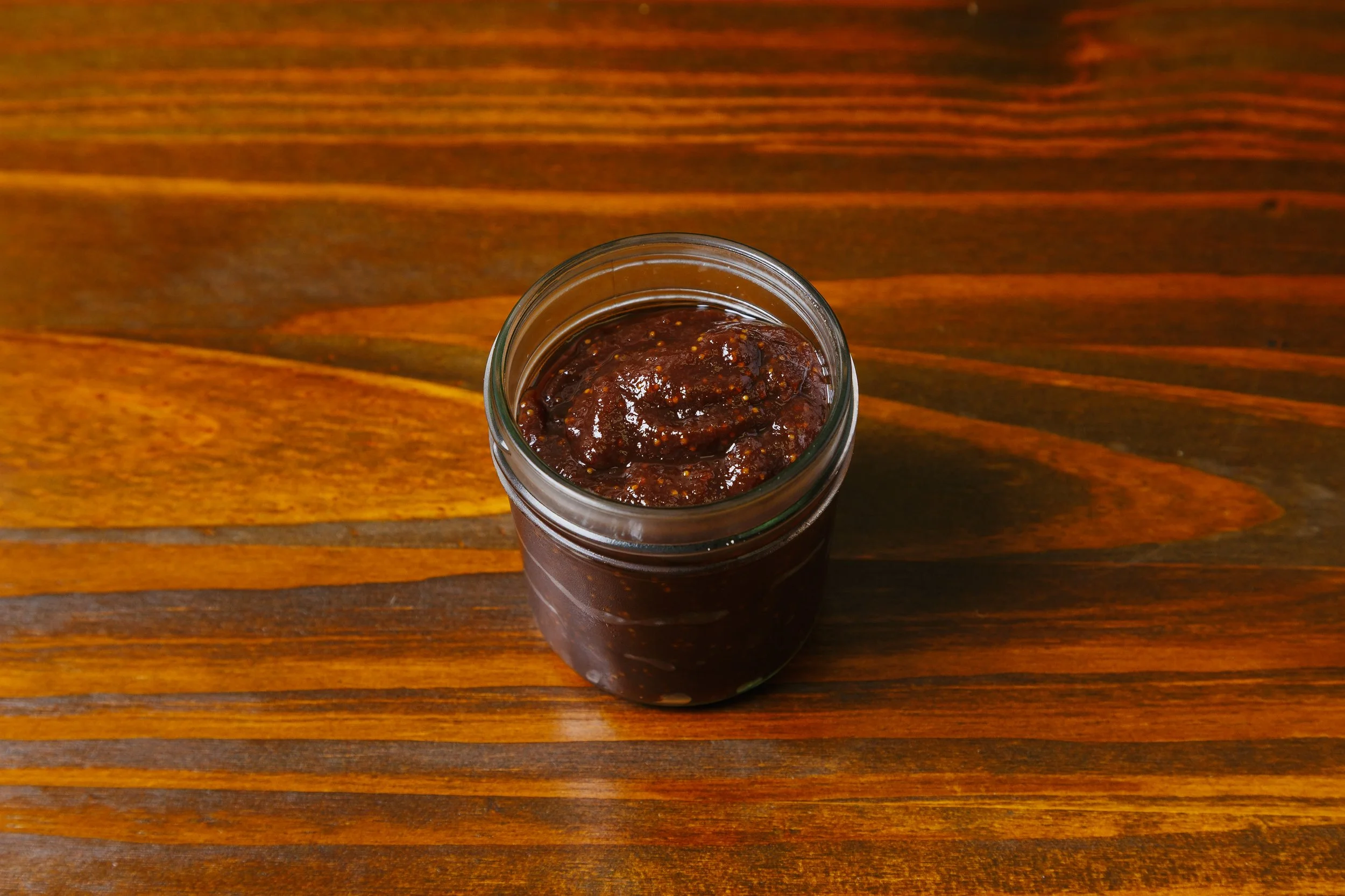 A jar of dark red chili paste on a wooden surface.