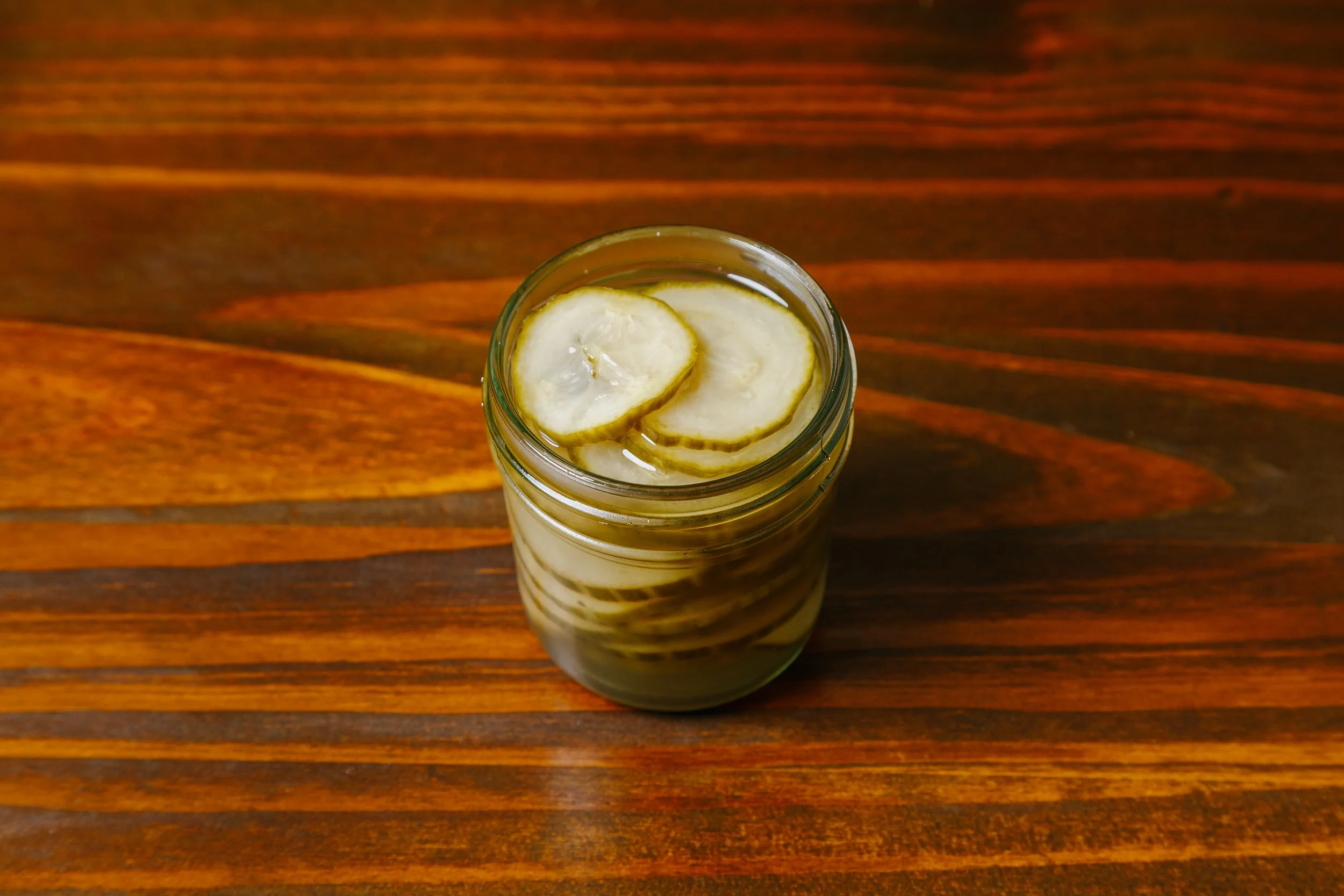 A jar with sliced bananas inside served in a liquid on a wooden surface.