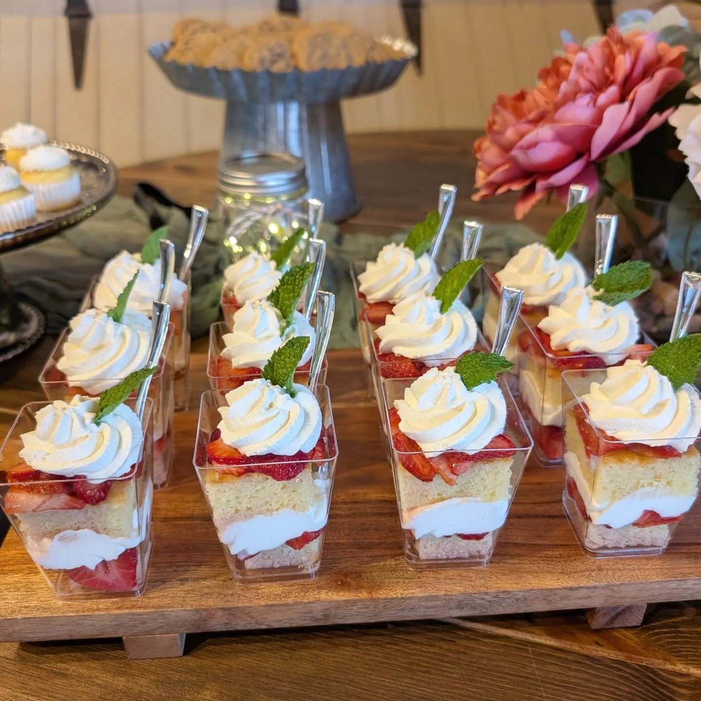Individual strawberry shortcake desserts topped with whipped cream and mint leaves, arranged on a wooden serving tray.