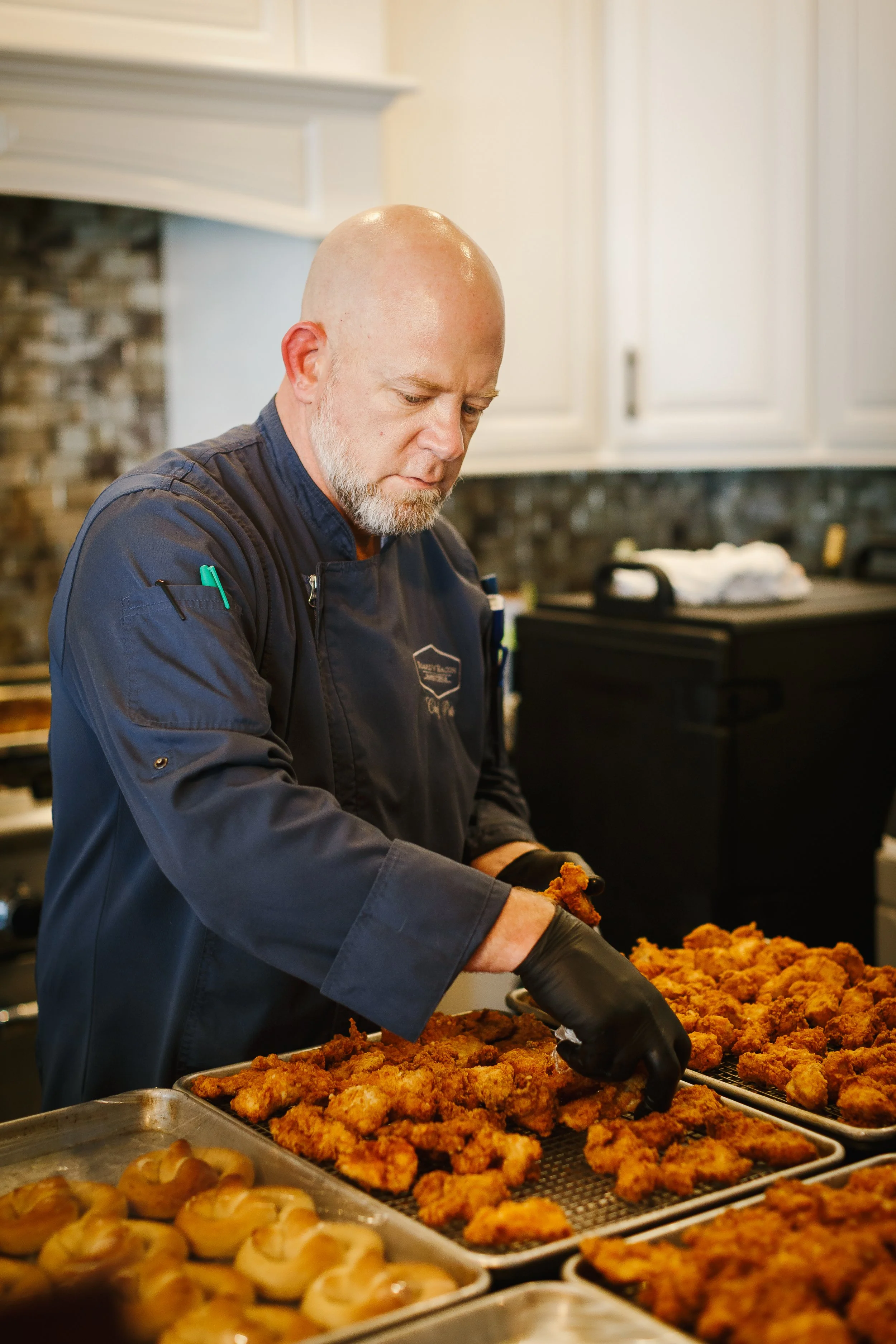 A chef in a black uniform preparing fried chicken on a baking sheet in a kitchen.