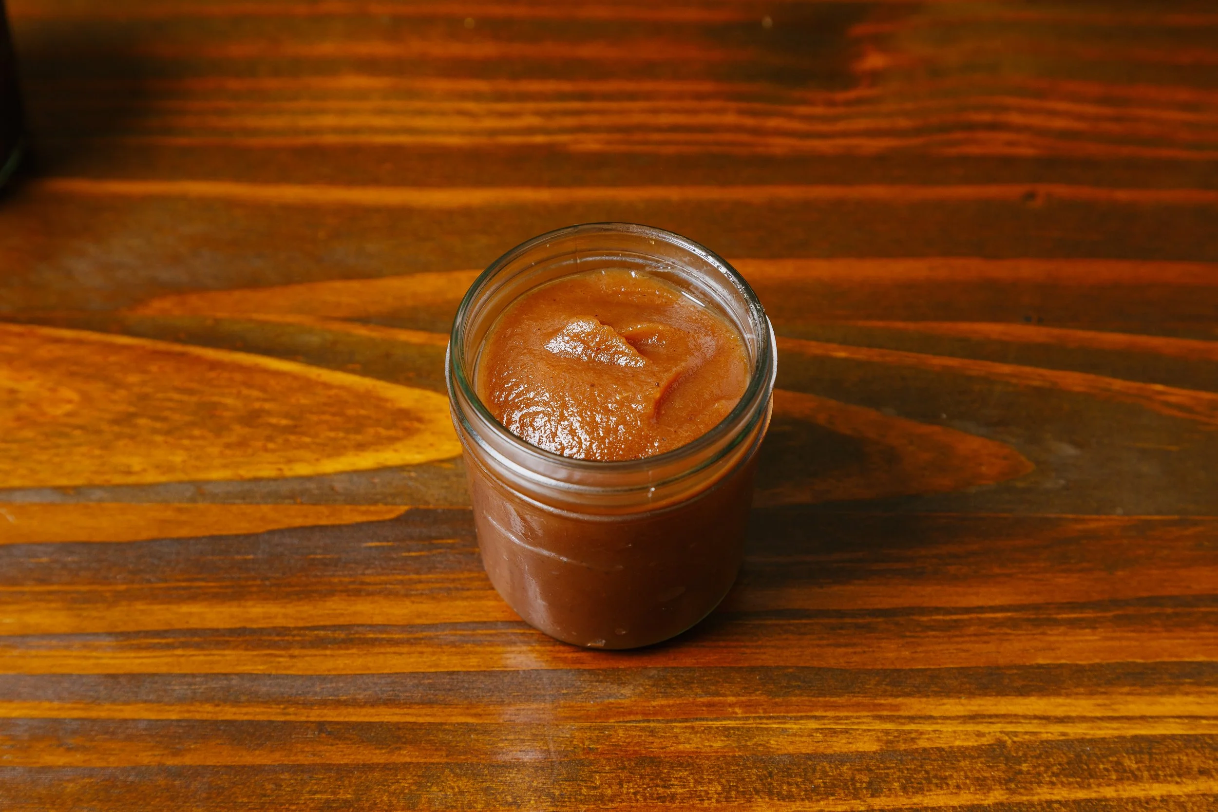 A jar filled with brown caramel sauce on a wooden surface.