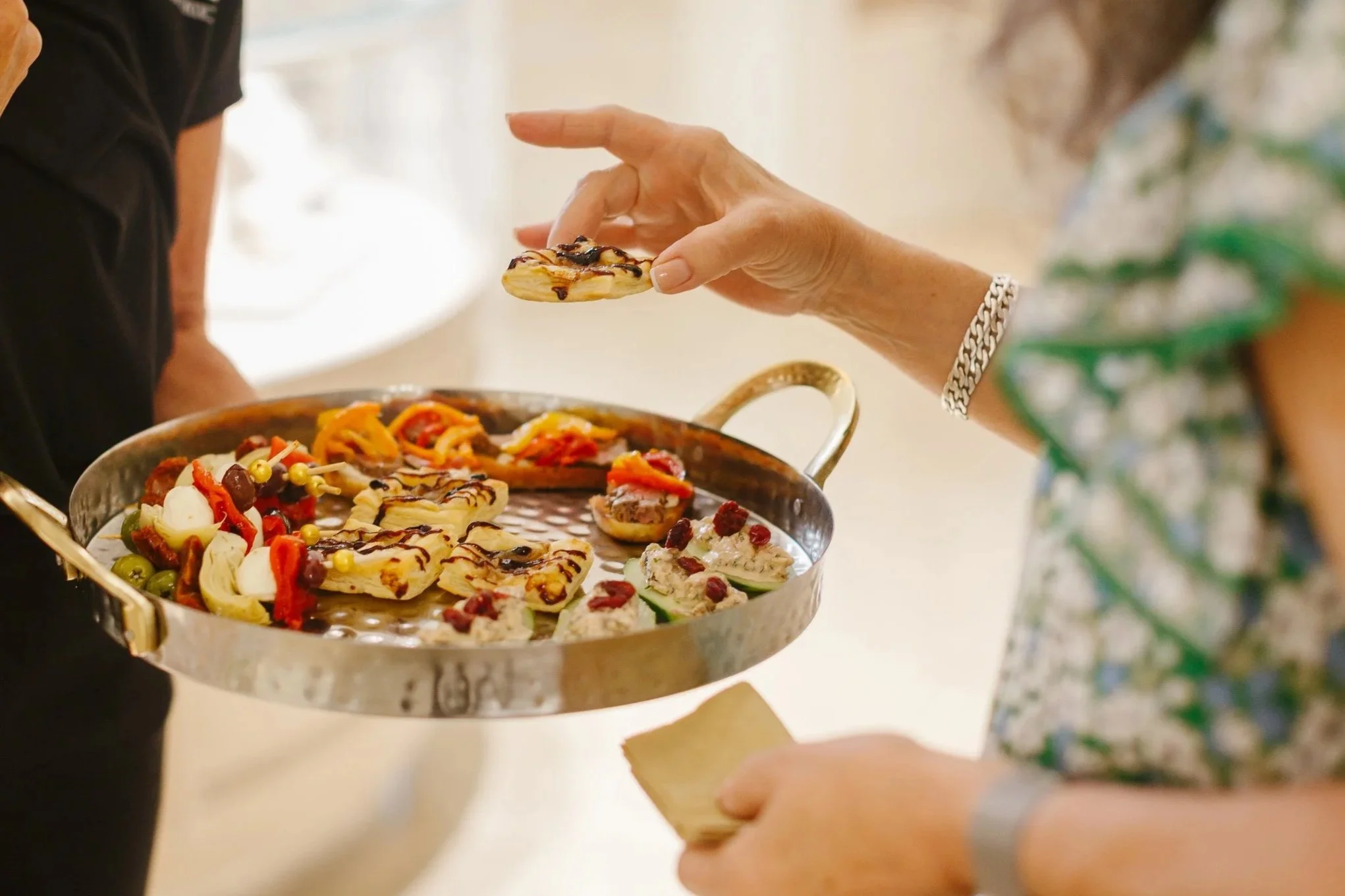 Person serving bites of colorful, decorated miniature pastries from a tray at a gathering.